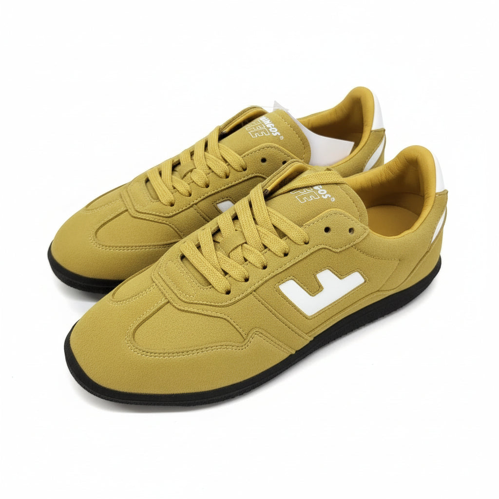 Ein Paar gelbe Turnschuhe mit weißen Akzenten und schwarzen Sohlen, die auf einer hellgrauen Oberfläche abgebildet sind. Die Schuhe haben ein weißes L-Design an den Seiten und gelbe Schnürsenkel.