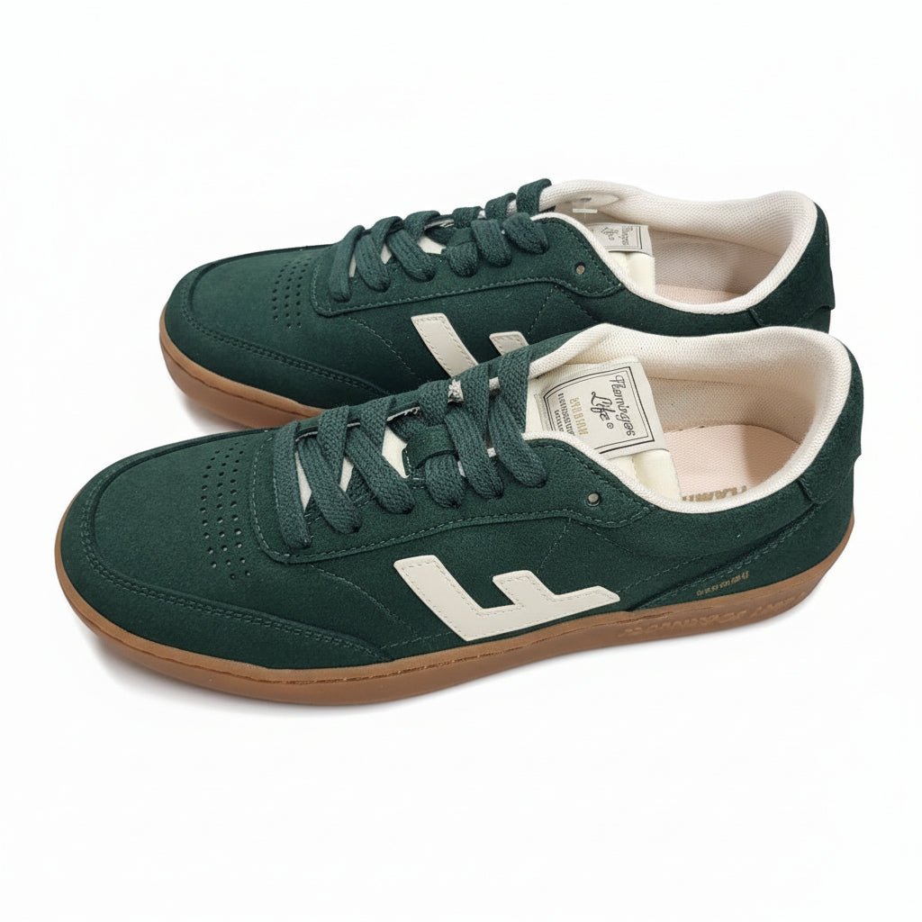 Ein Paar grüne Wildleder-Sneaker mit weißen Akzenten, cremefarbenen Seitenlogos und Gummisohlen stehen auf einem grauen Betonboden.