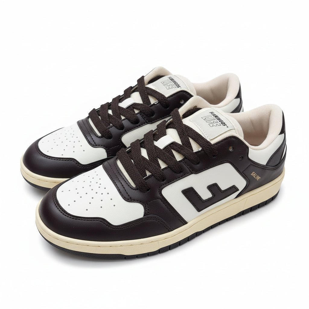 Ein Paar schwarz-weiße Turnschuhe mit cremefarbenen Sohlen auf einem grauen Betonboden; die Schuhe tragen den Buchstaben E an der Seite und schwarze Schnürsenkel.