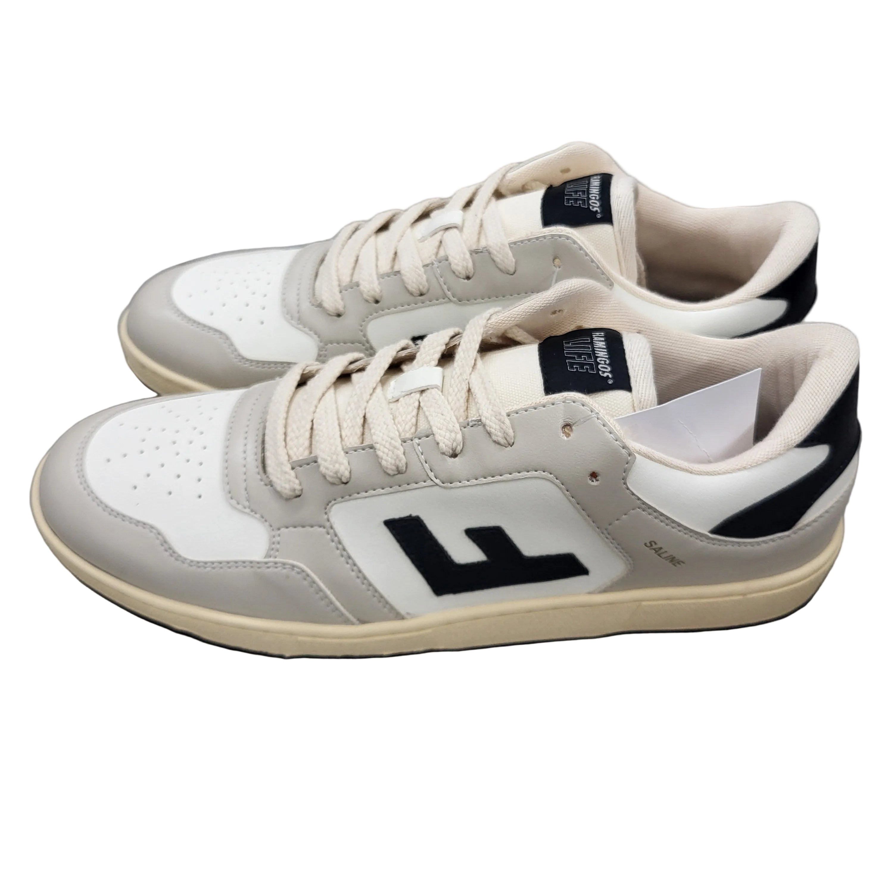 Ein Paar Turnschuhe mit cremefarbenen Schnürsenkeln, weißem Obermaterial, hellgrauen Akzenten, schwarzer Laufsohle und einem großen schwarzen F-Logo an der Seite, die auf einem grauen Betonboden stehen.