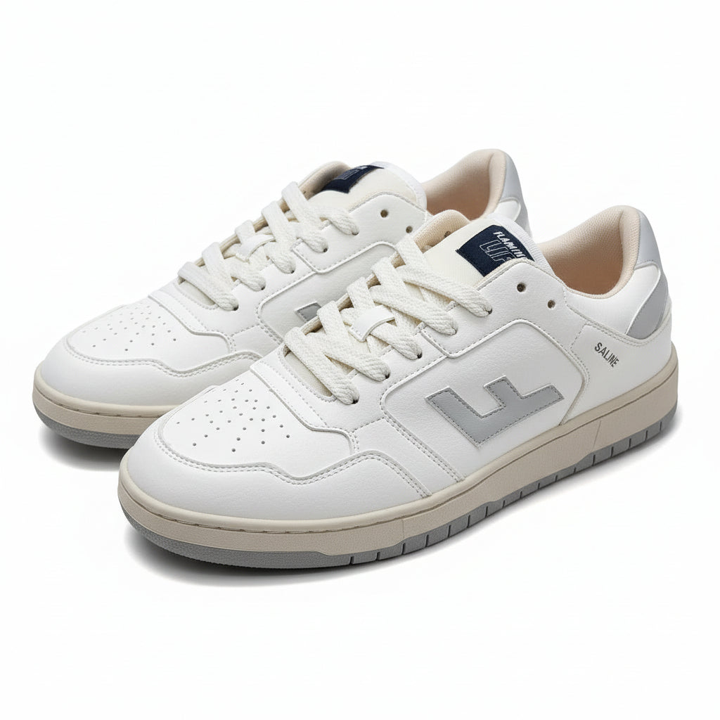 Ein Paar weiße Turnschuhe mit hellgrauen Akzenten und beigem Innenfutter, mit einem großen "L"-Logo an der Seite und dem Wort "SALVIE" in der Nähe der Ferse, das auf einer grauen Oberfläche aufliegt.