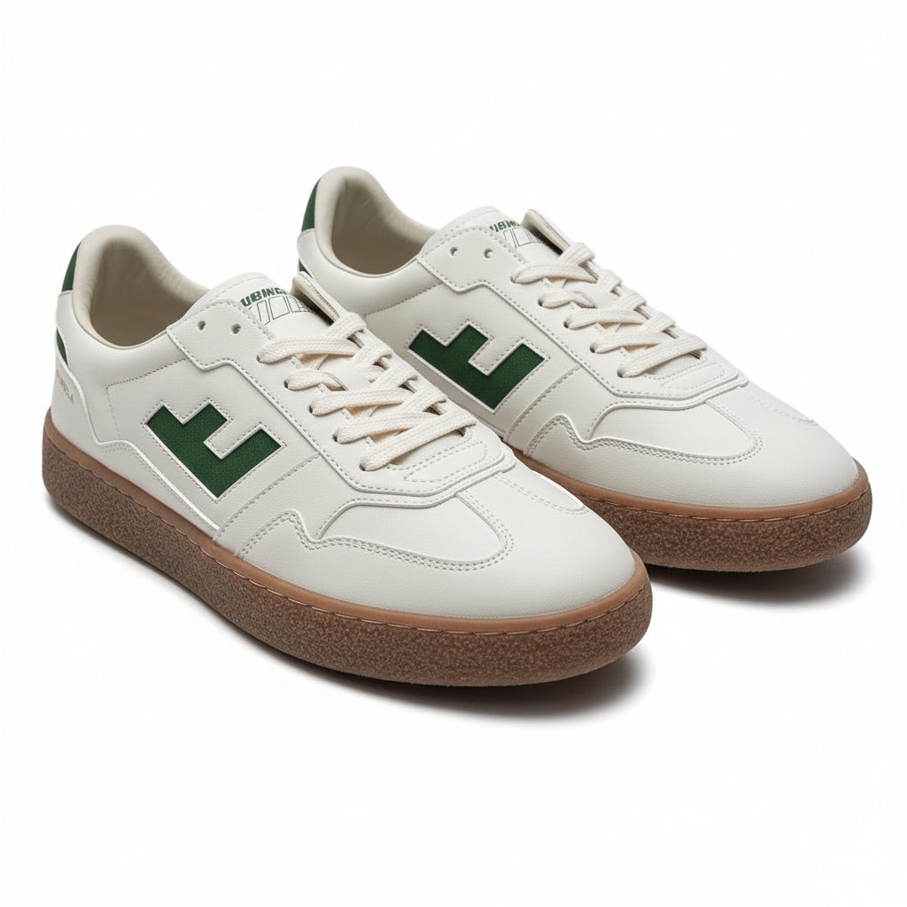 Ein Paar weiße Turnschuhe mit grünen Akzenten, Gummisohlen und dem Wort BURELA an der Ferse. Die Schuhe stehen auf einem grauen, glatten Boden.