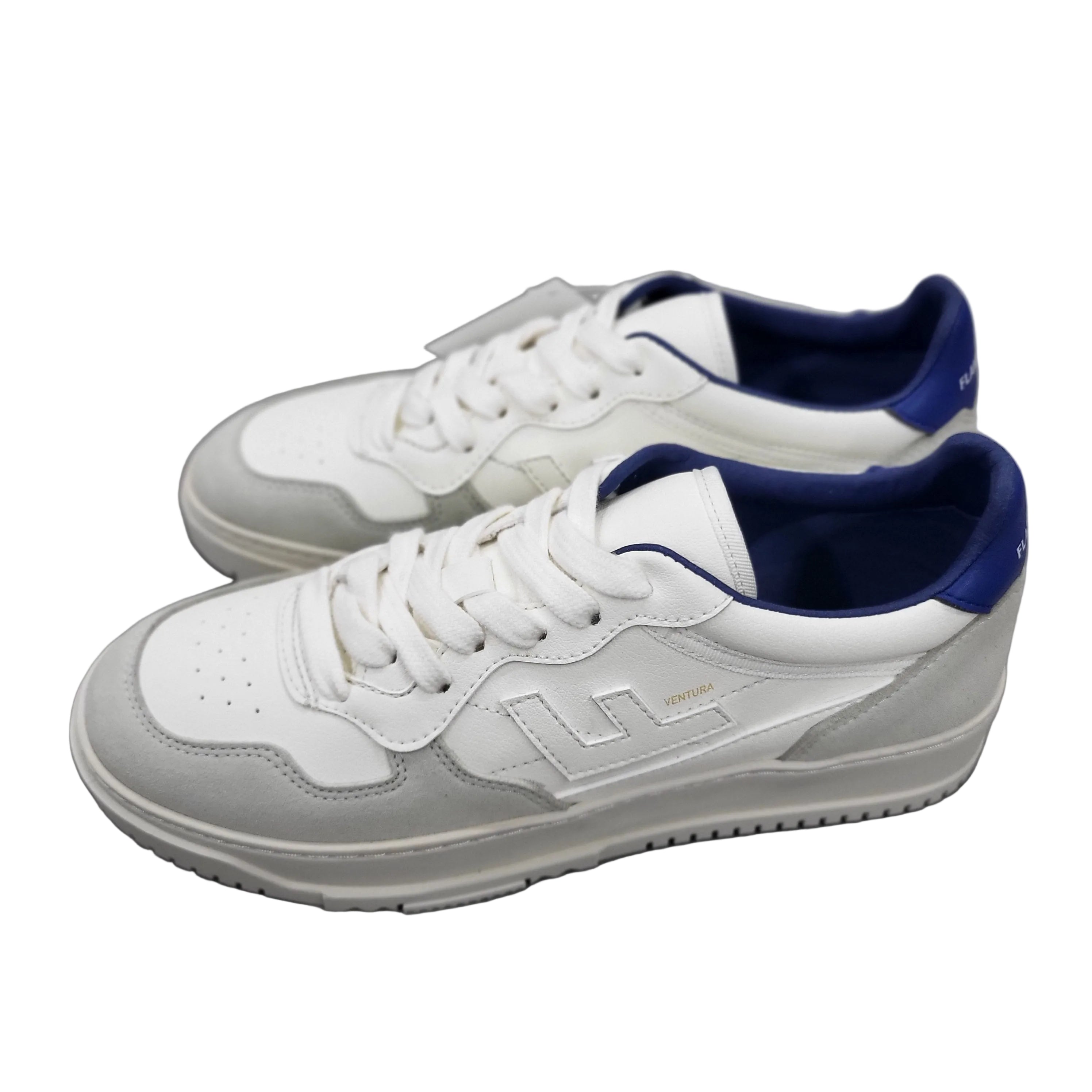 Ein Paar weiße und hellgraue Turnschuhe mit marineblauem Innenfutter und der Aufschrift VENEDA an der Seite, die auf einem grauen Betonboden stehen.