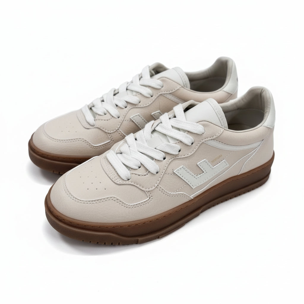 Ein Paar weiße Ledersneaker mit beigen Akzenten, weißen Schnürsenkeln, Gummisohlen und aufgenähten Logodetails an der Seite, die auf einer grauen Betonfläche stehen.