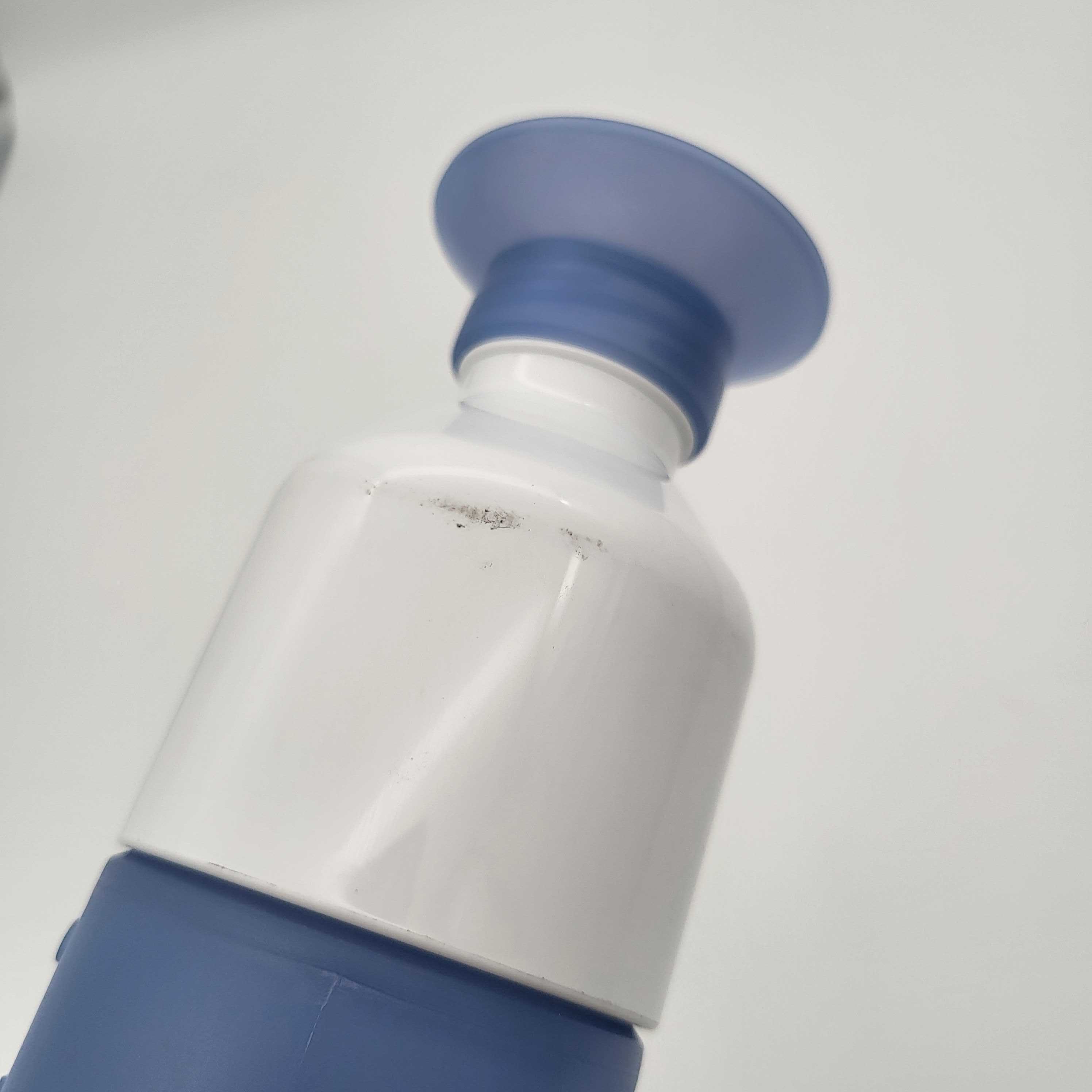 Nahaufnahme einer weiß-blauen Plastikflasche mit einem breiten, flachen Deckel vor einem schlichten, hellen Hintergrund.