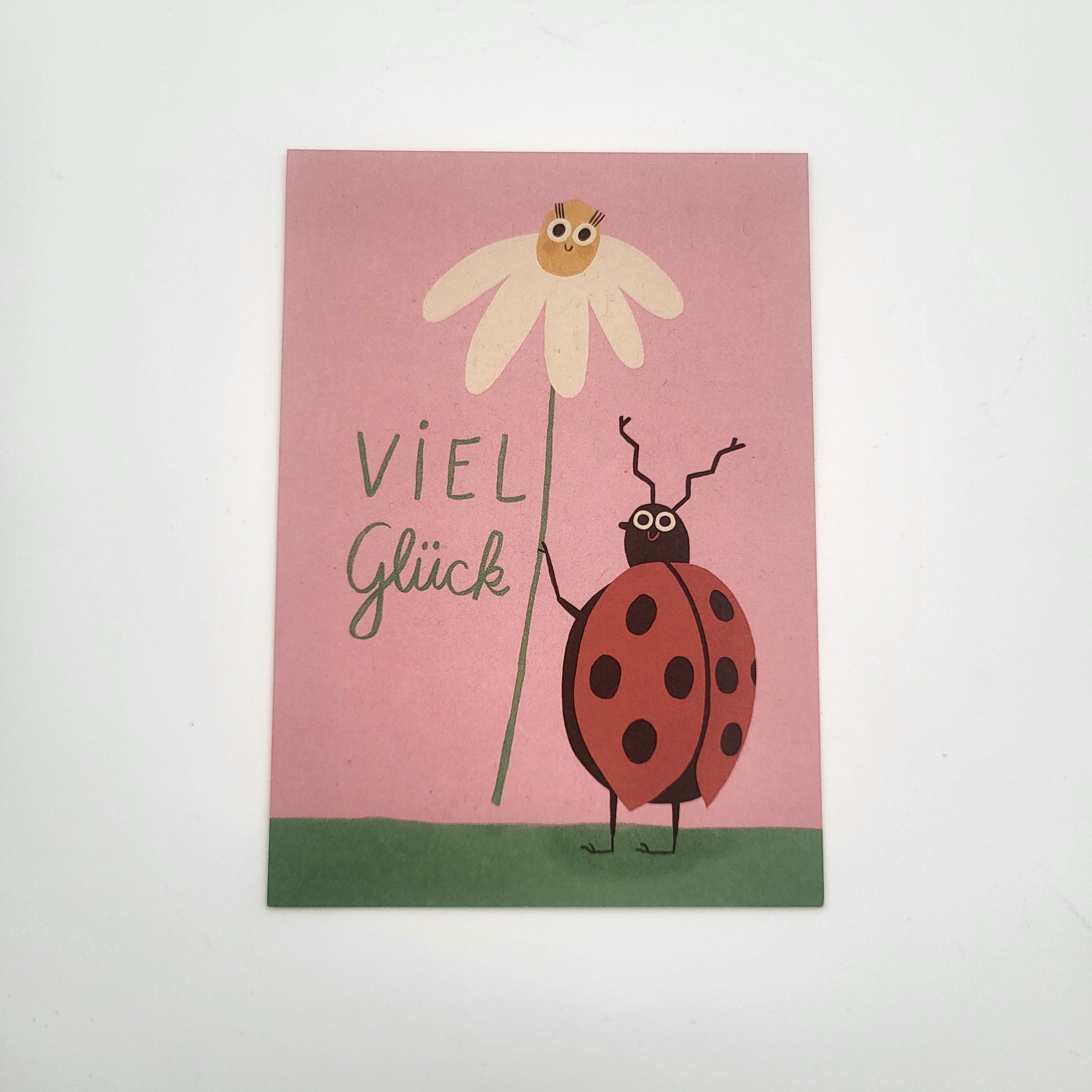 Eine Grußkarte mit rosa Hintergrund zeigt einen Marienkäfer, der eine weiße Blume hält, auf der eine lächelnde Biene sitzt. Neben dem Marienkäfer stehen die Worte Viel Glück geschrieben.