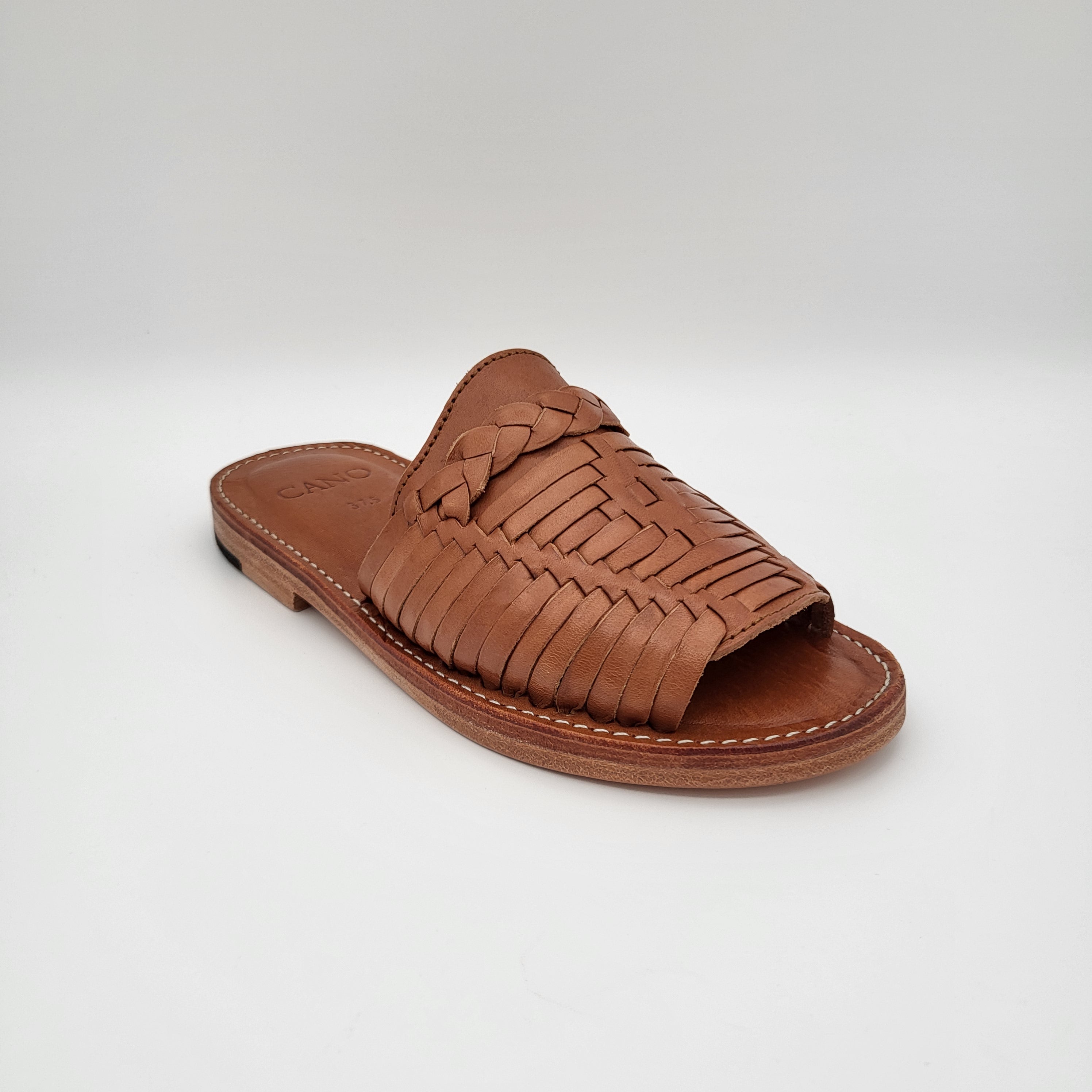 Braune Pantolette aus geflochtenem Leder mit offener Zehenpartie, flacher Sohle und geflochtenen Details auf dem Obermaterial vor einem schlichten weißen Hintergrund.