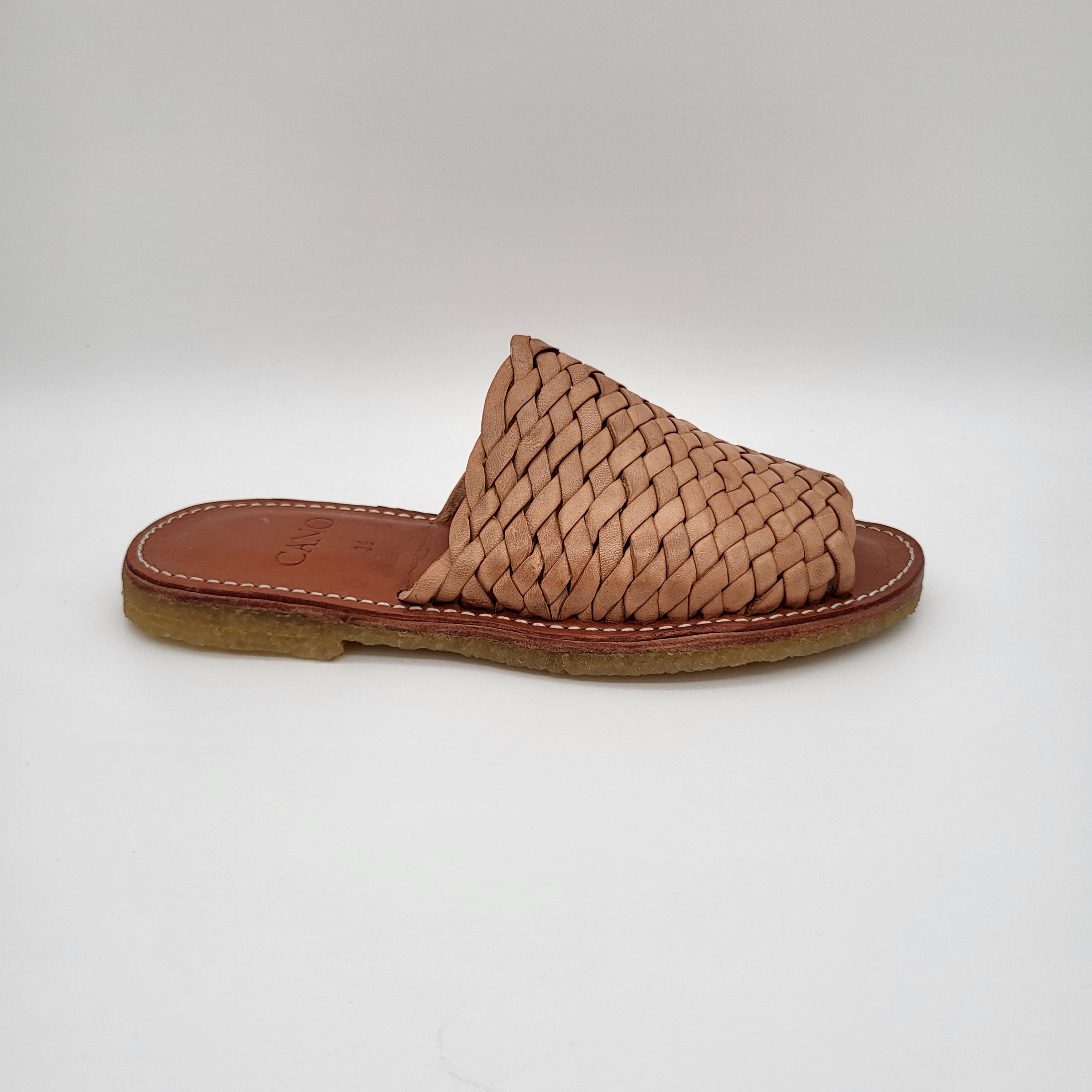 Hellbraune Ledersandale mit geflochtenem Obermaterial und flacher Sohle, die vor einem schlichten weißen Hintergrund steht.