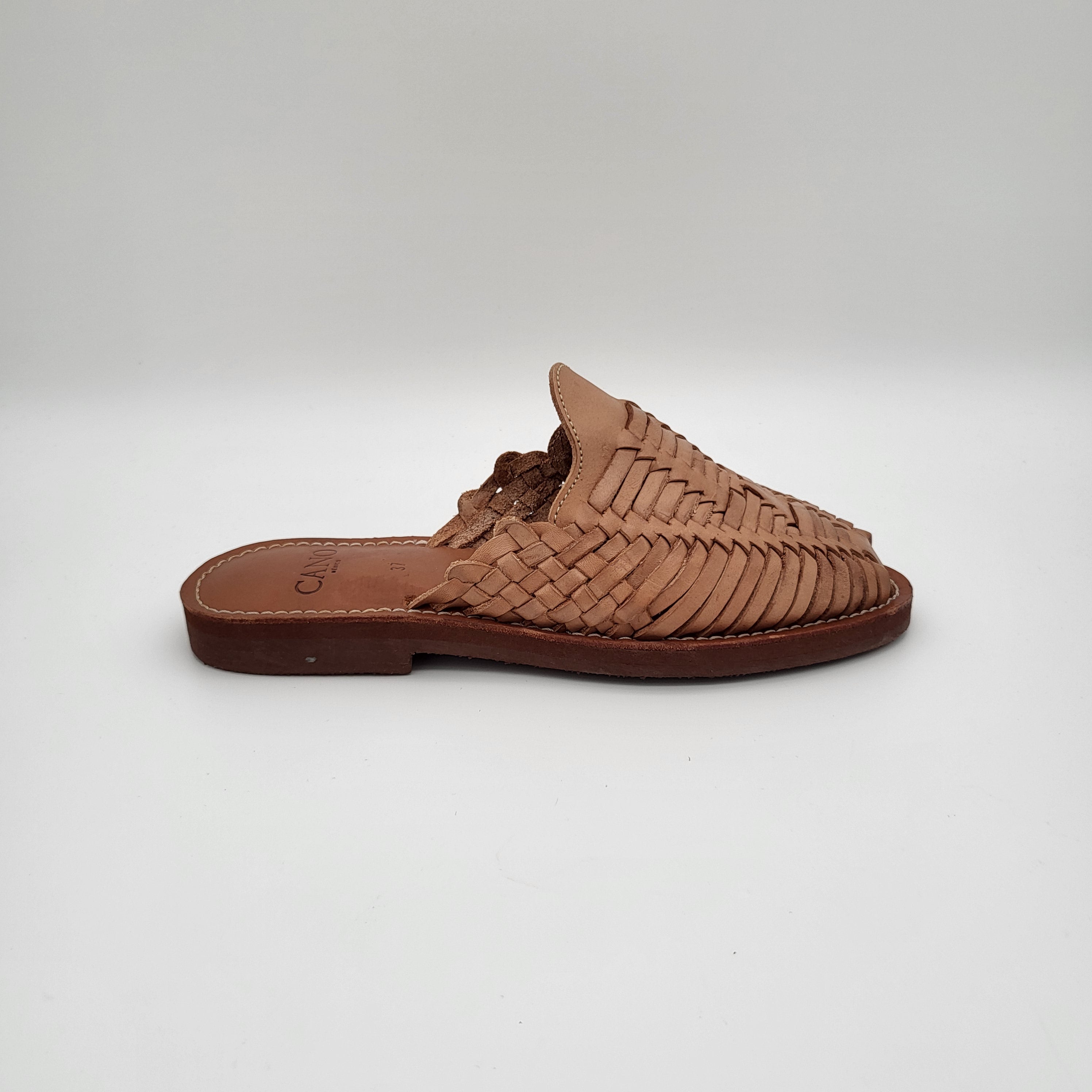 Eine einzelne hellbraune Slipper-Sandale aus gewebtem Leder mit flacher Sohle, die vor einem schlichten weißen Hintergrund steht.