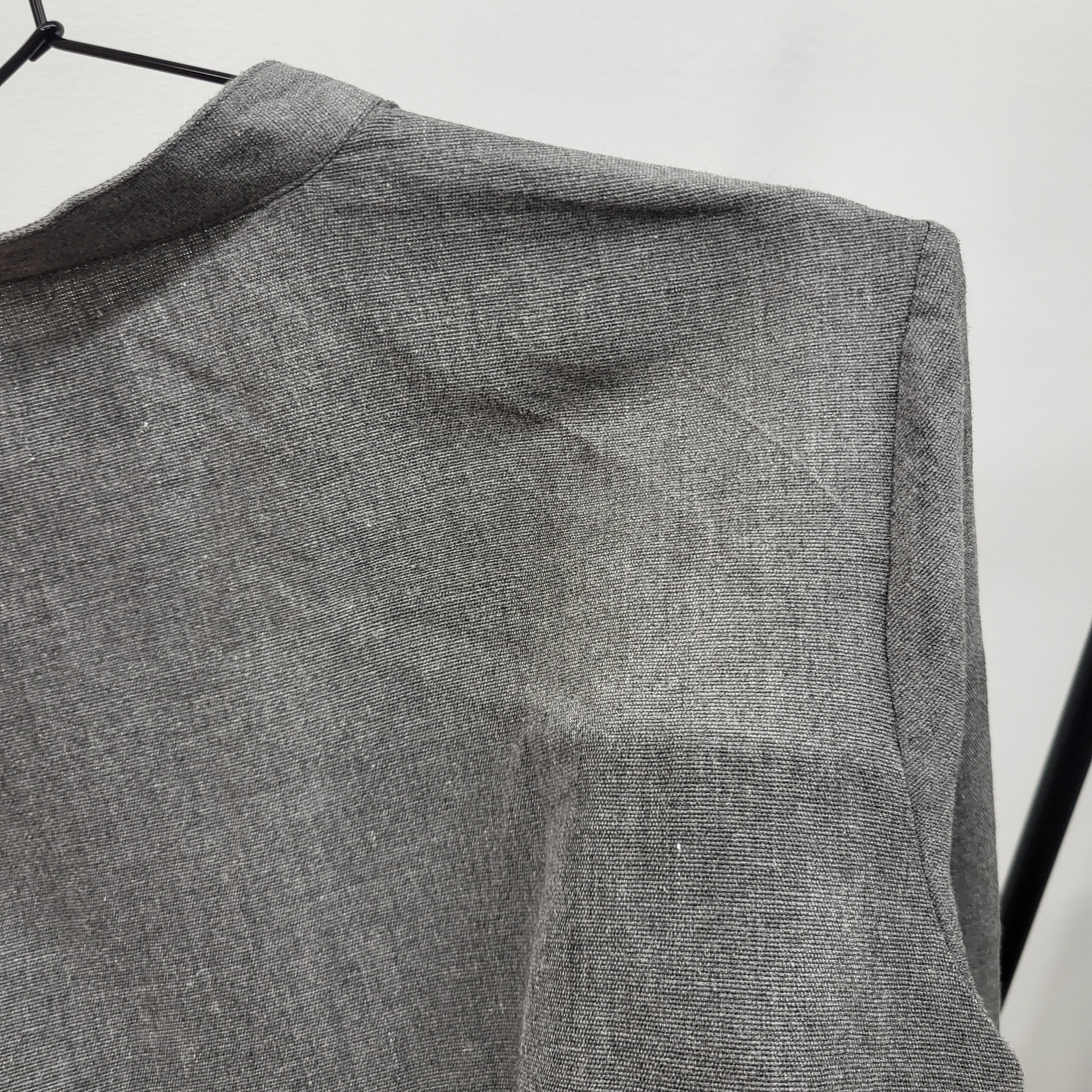 Nahaufnahme der Schulter und des oberen Ärmelbereichs eines auf einem Bügel hängenden grauen Leinenkleidungsstücks, die die Textur des Stoffes und die feinen Falten zeigt.