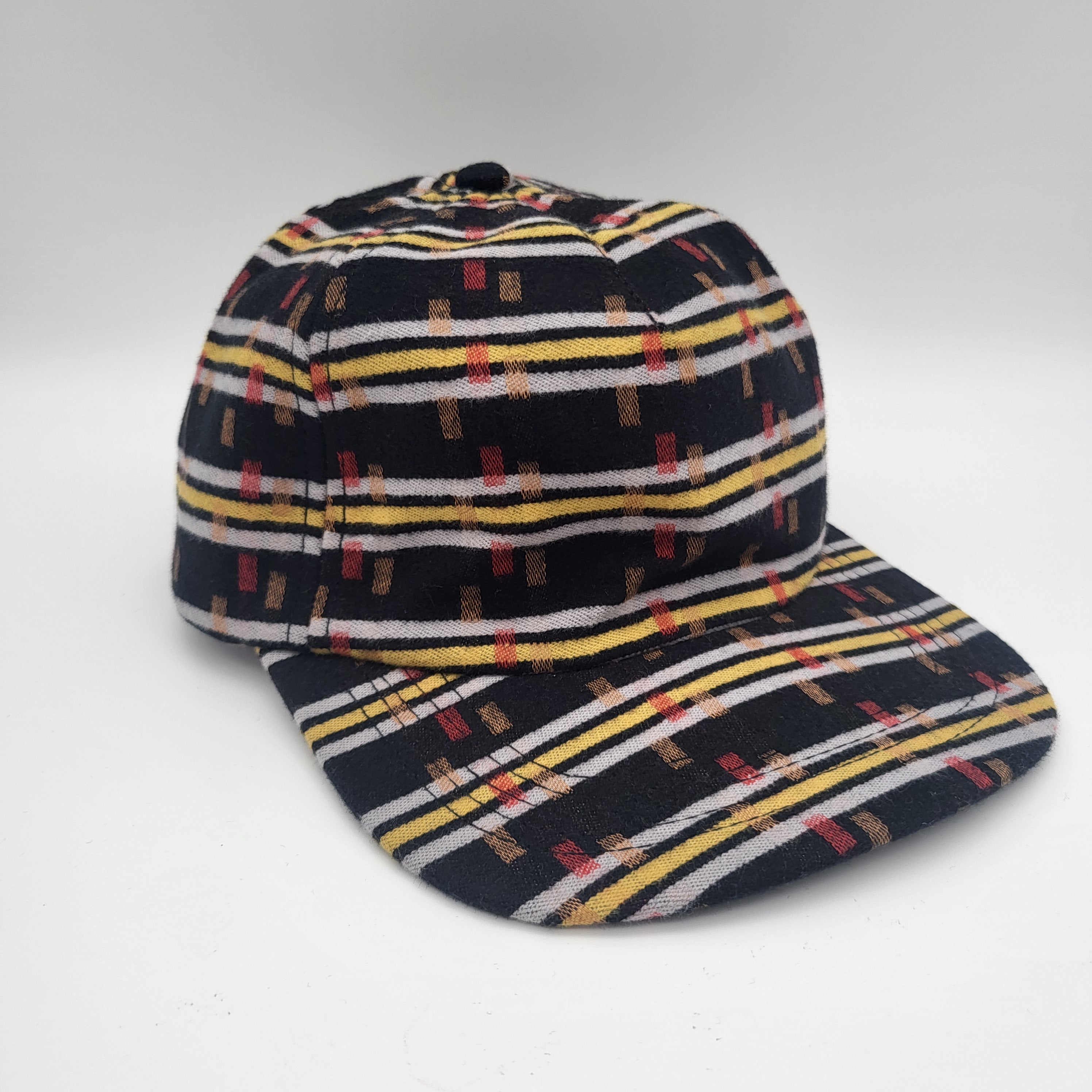 Eine mehrfarbige Baseballkappe mit schwarzer Basis und horizontalen Streifen in Gelb, Weiß und Rot, die ein geometrisches rechteckiges Muster aufweisen. Die Kappe ist auf einem schlichten weißen Hintergrund abgebildet.
