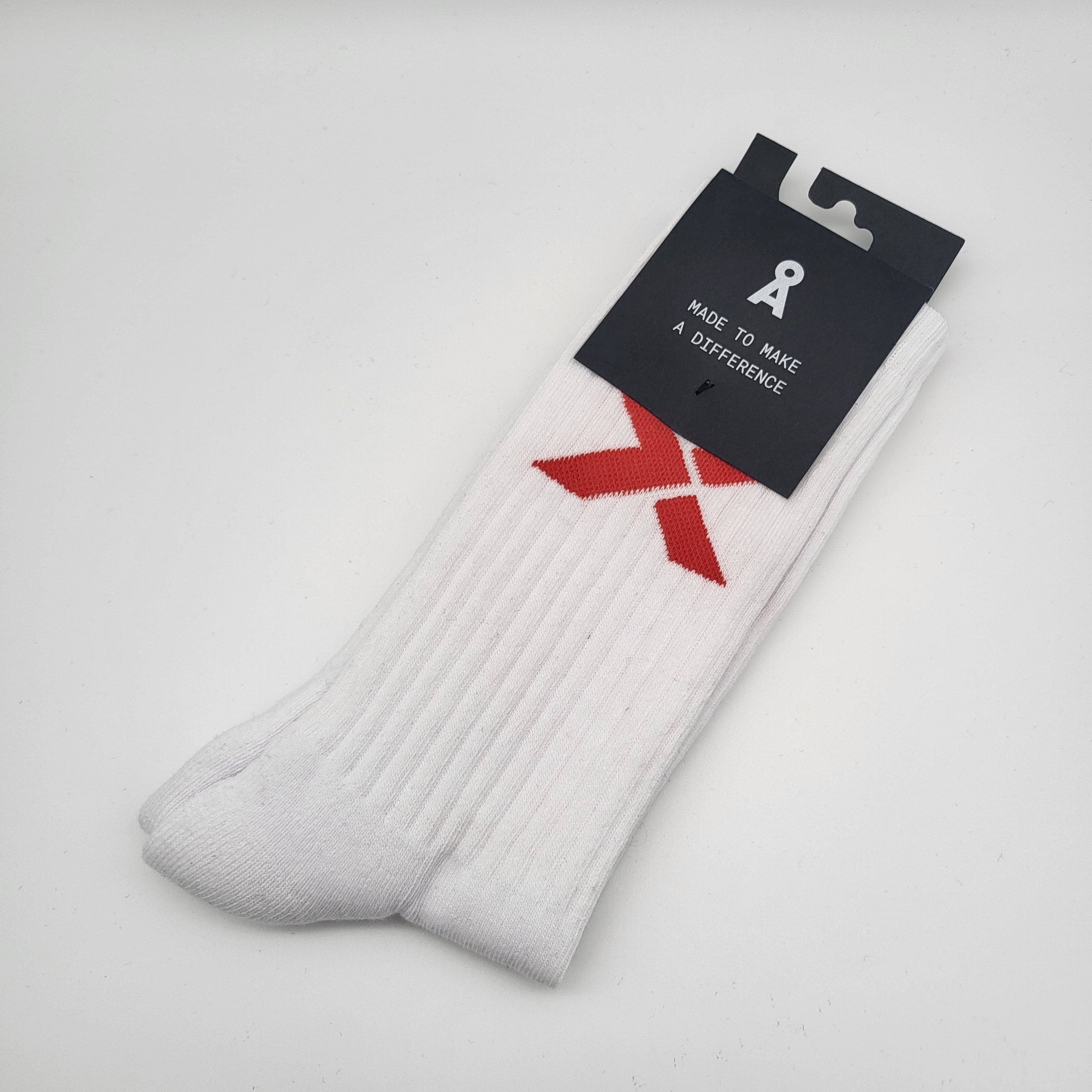 Ein Paar weiße gerippte Socken mit einer roten Schleife am oberen Rand, verpackt mit einem schwarzen Schild mit der Aufschrift "MADE TO MAKE A DIFFERENCE". Die Socken sind auf einem schlichten weißen Hintergrund abgebildet.