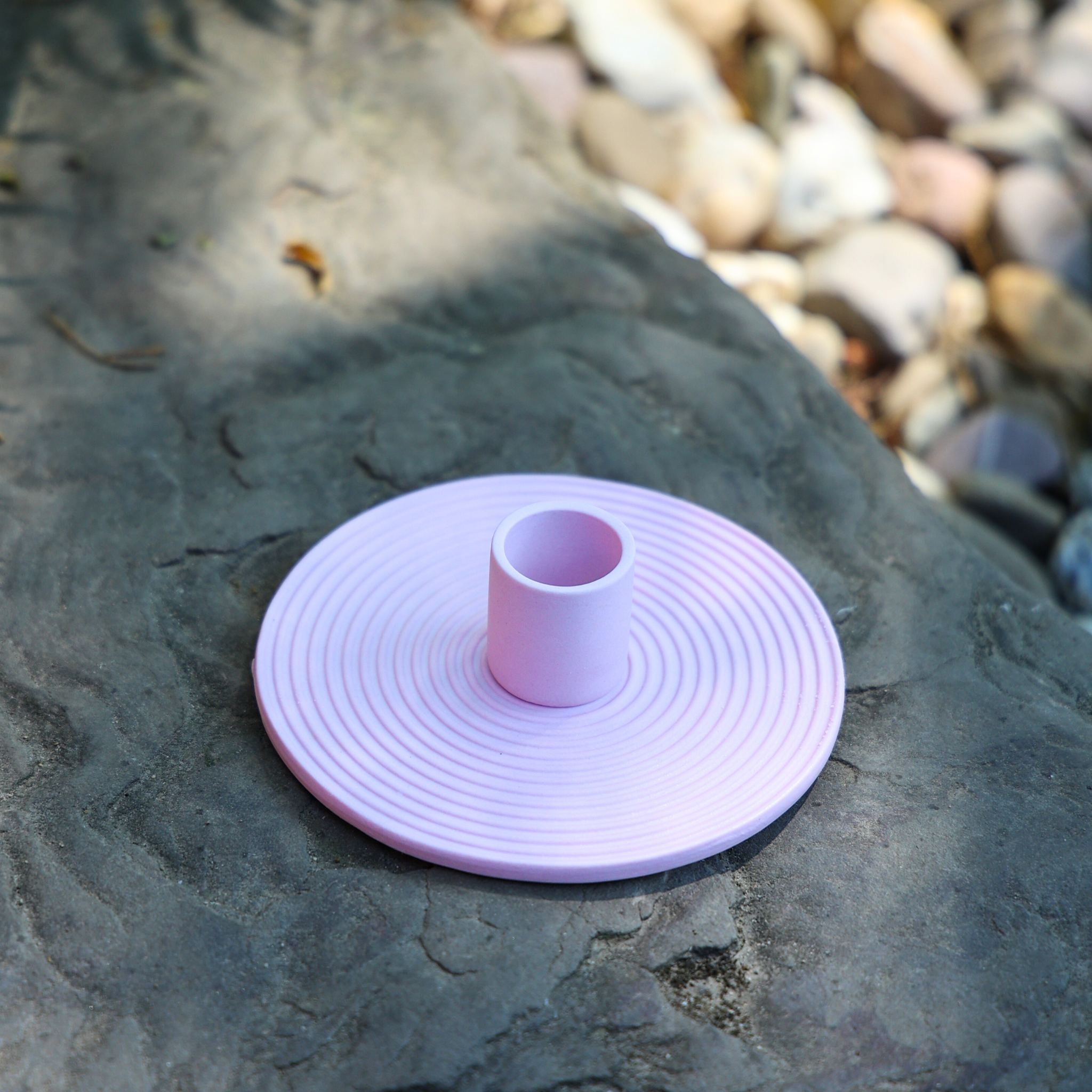 Ein rosafarbenes, kreisförmiges, geriffeltes Objekt mit einem zylindrischen Zentrum sitzt auf einem großen grauen Stein im Freien, mit unscharfen Kieselsteinen im Hintergrund.