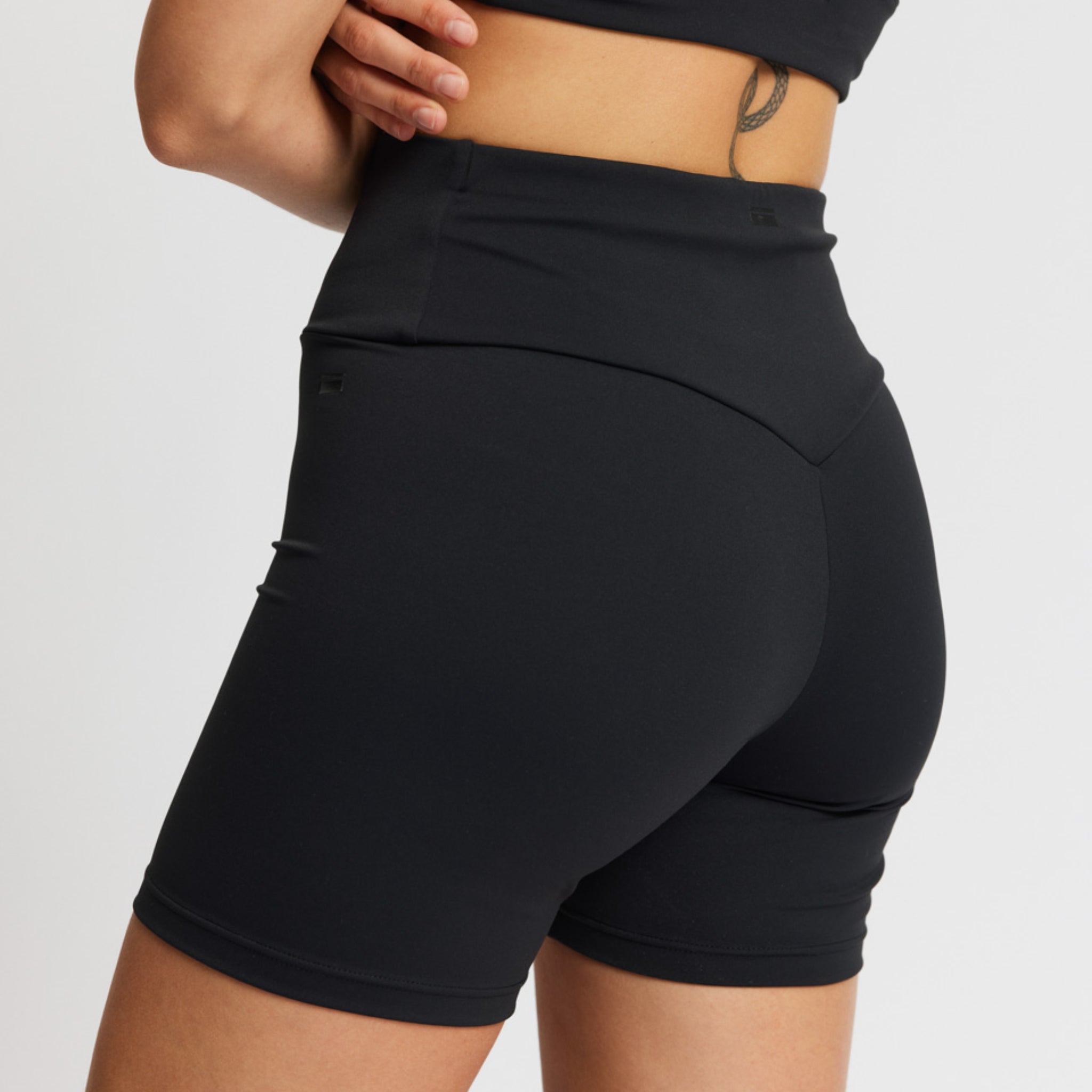 Eine Person trägt schwarze, hochgeschnittene Sportshorts, an der Seite ist ein Tattoo zu sehen.