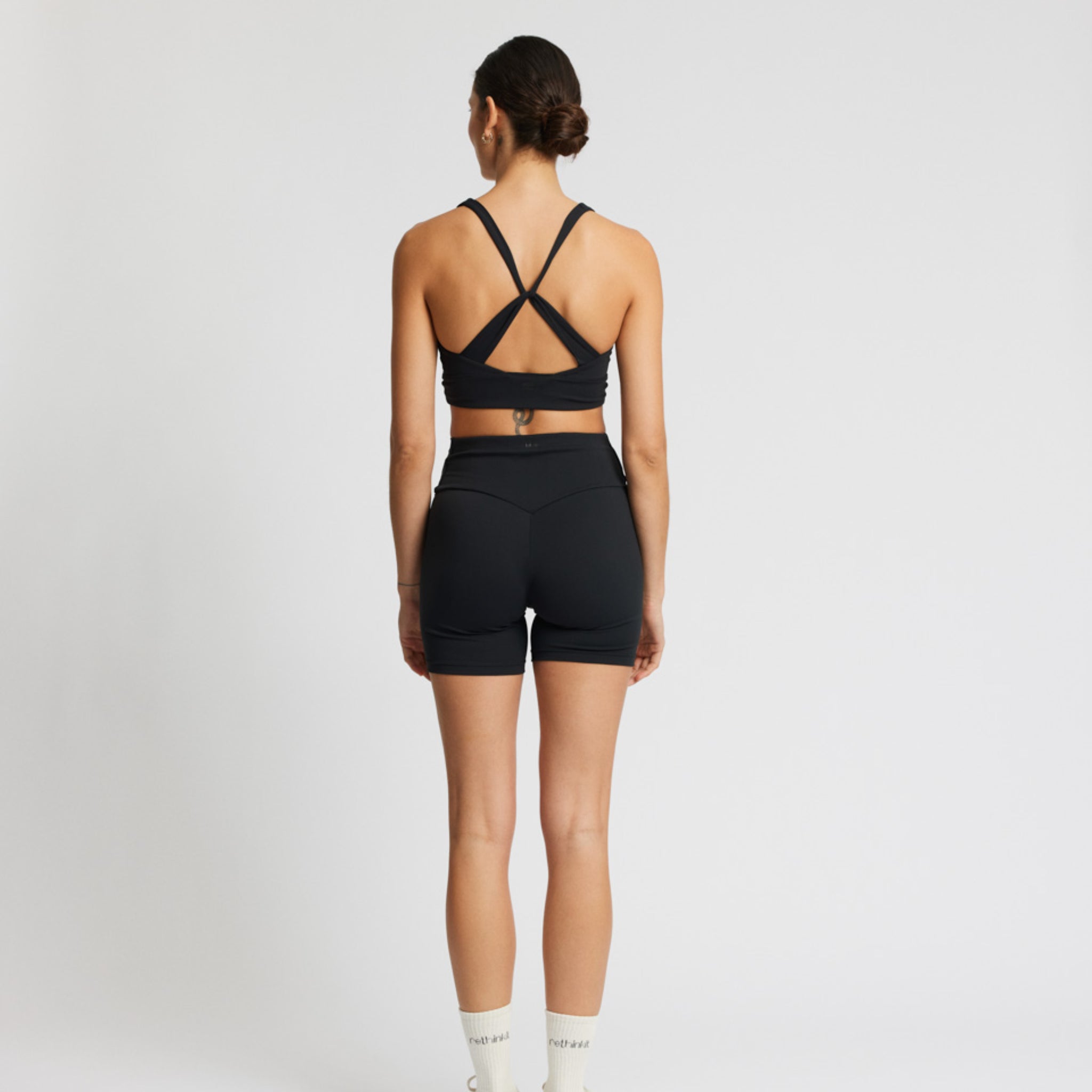 Eine Frau steht mit dem Rücken zur Kamera, trägt ein schwarzes Sport-Outfit und hat ihre Haare zu einem Dutt gebunden.