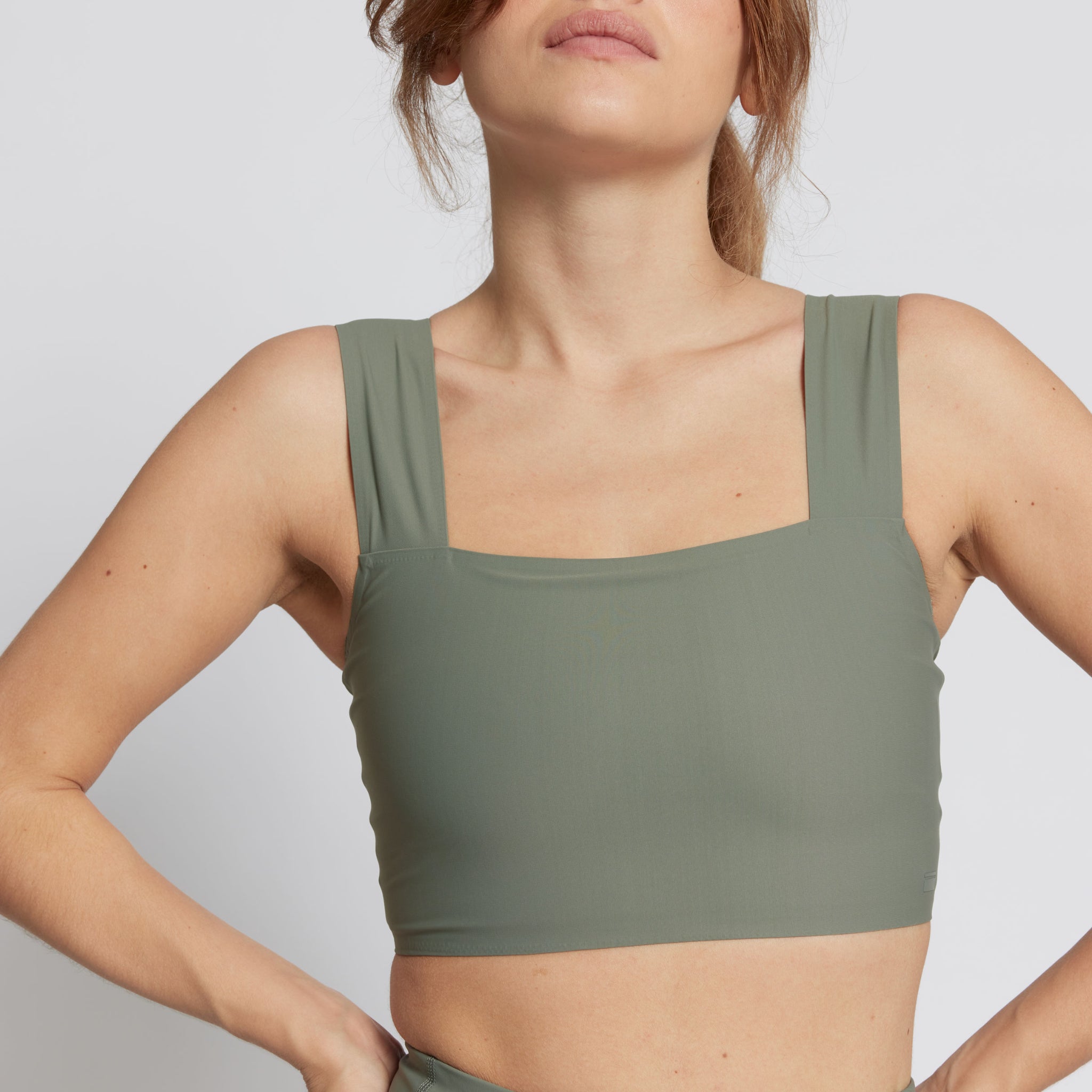 Eine Frau trägt ein olivgrünes Tanktop vor einem weißen Hintergrund.