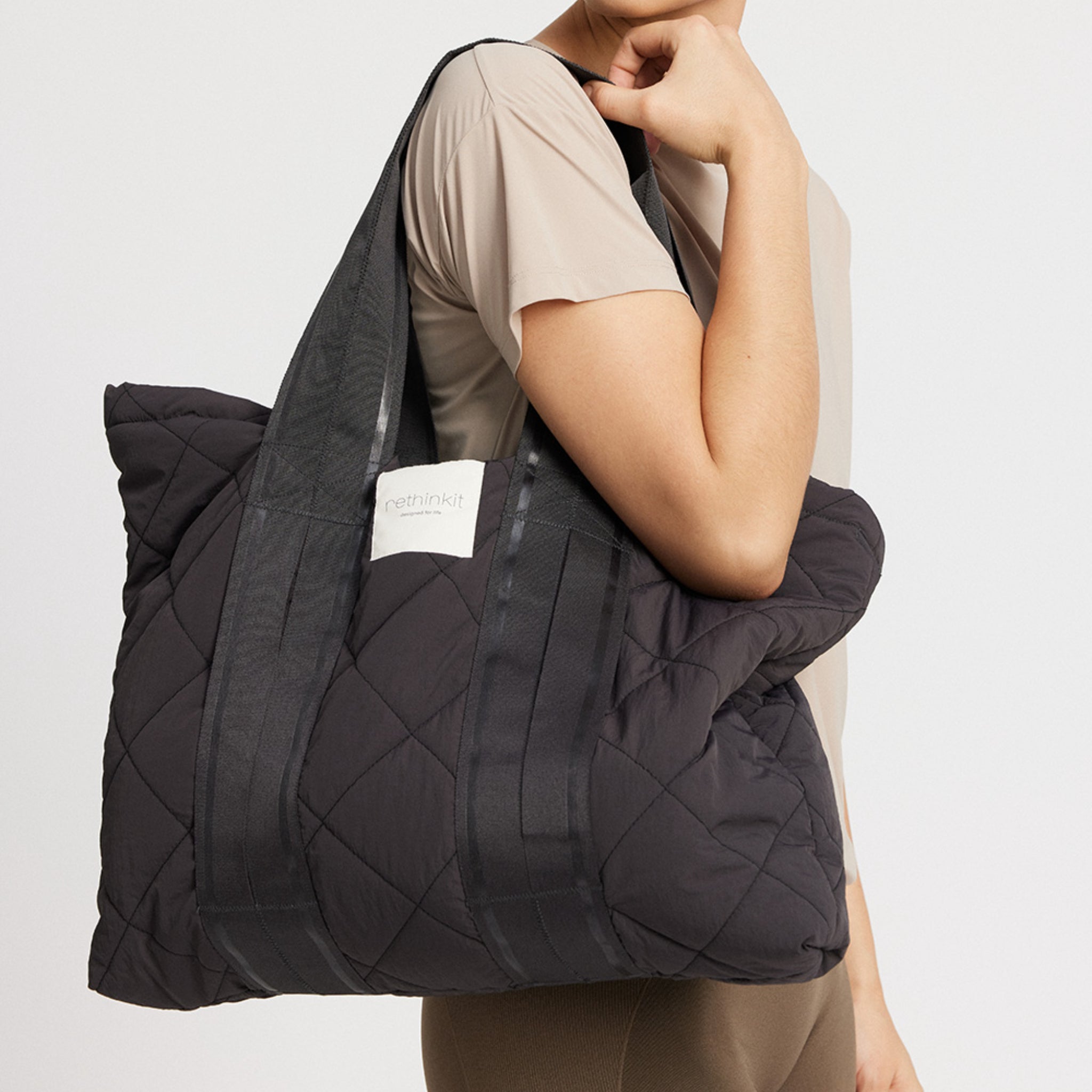 Person trägt eine große, gesteppte, schwarze Tasche mit einem Label "rethinkit" auf der Seite.