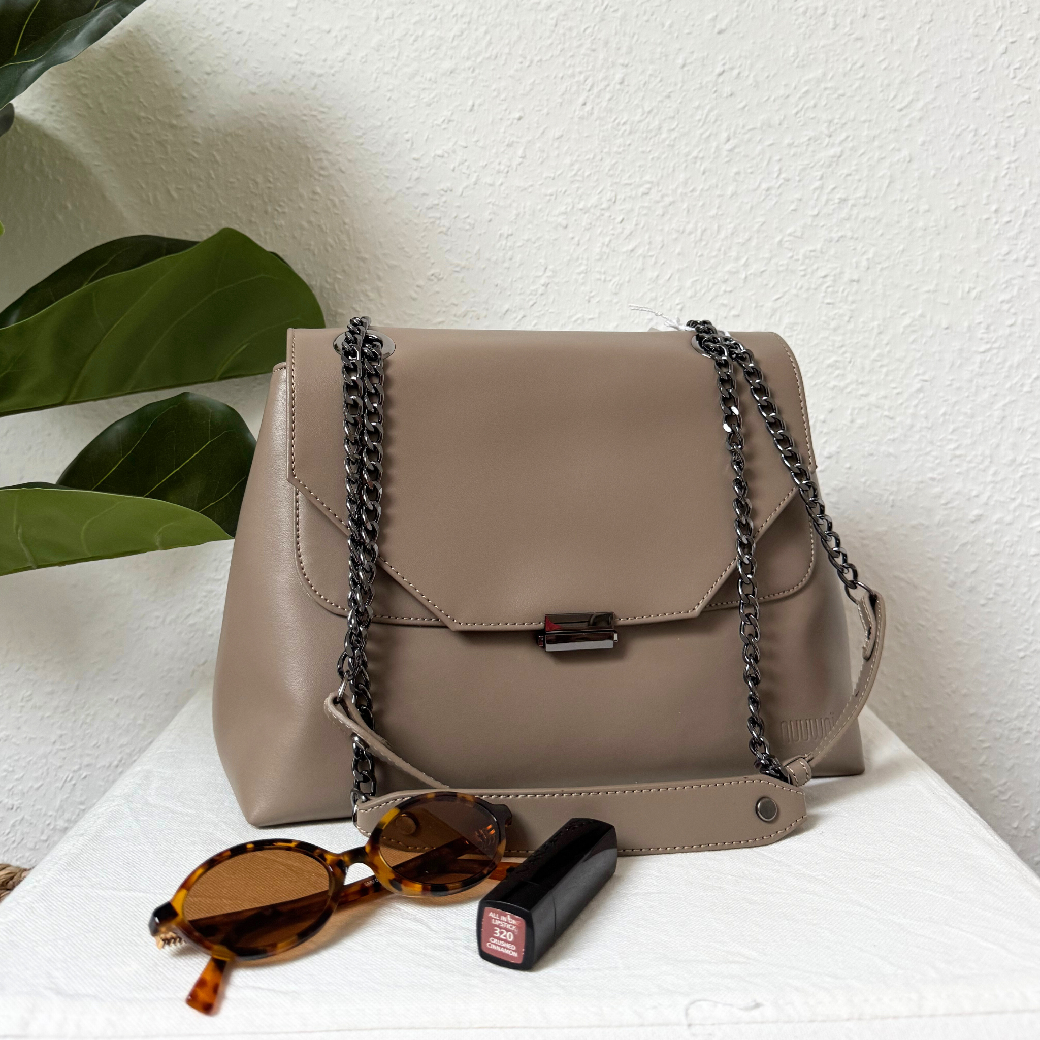 Beige Handtasche mit Kettengriff, daneben eine Sonnenbrille und ein Lippenstift auf einem hellen Hintergrund.