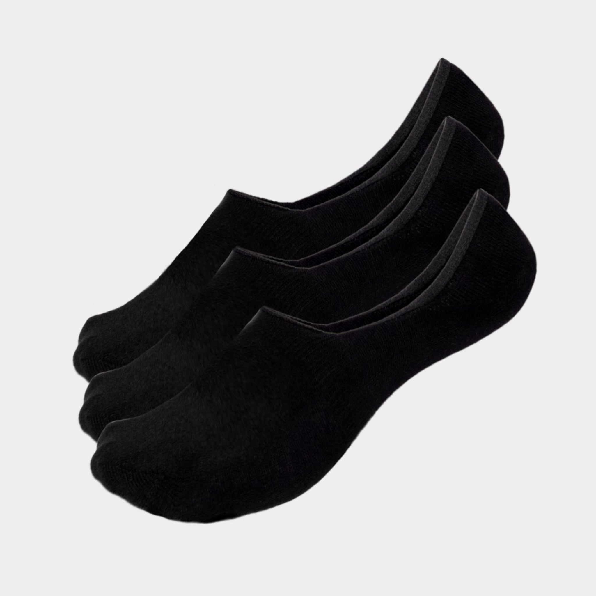 Drei Paar schwarze, flache Socken in einer Reihe auf hellgrauem Hintergrund.