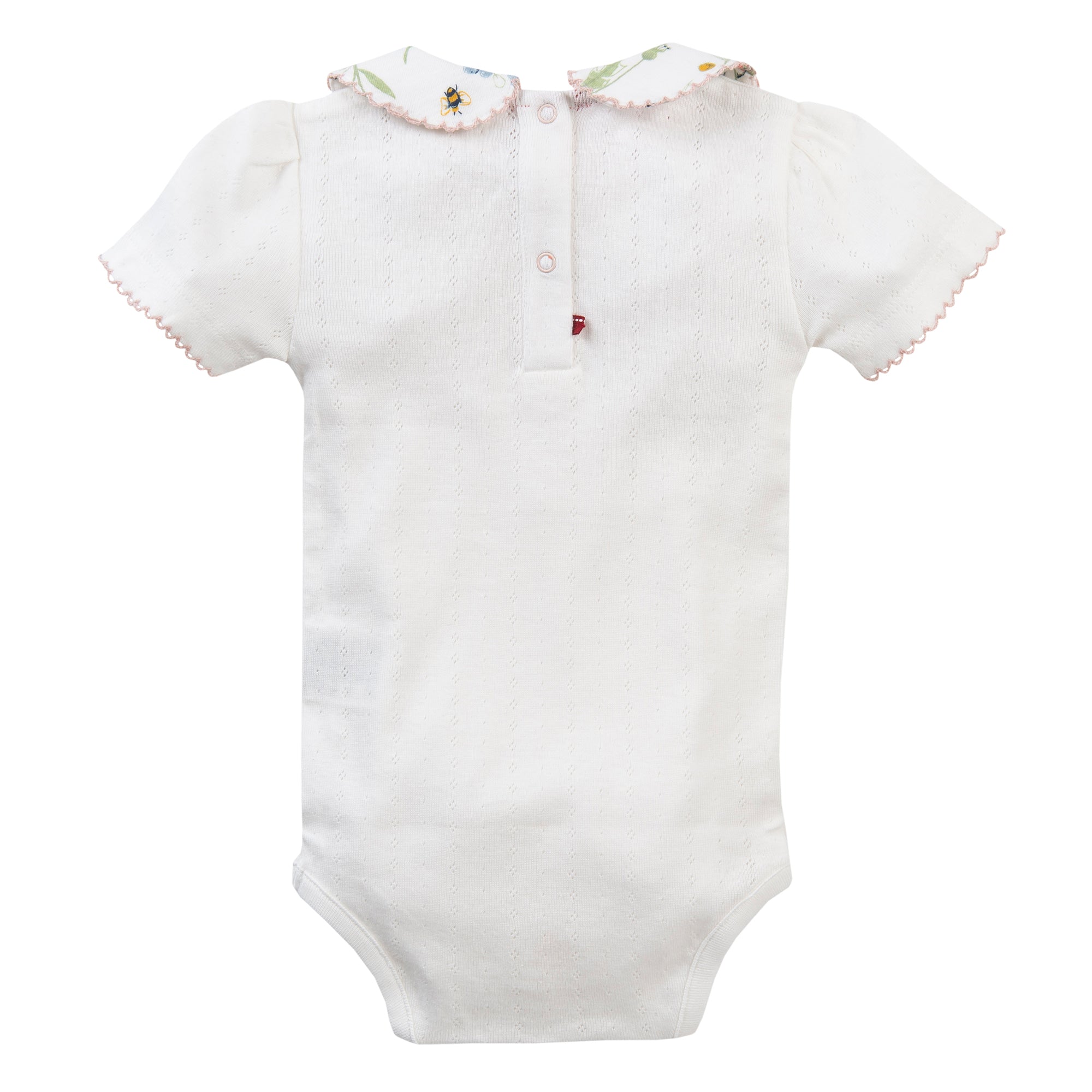 Weißer kurzärmeliger Baby-Strampler mit rosafarbenem Besatz an den Ärmeln und am Kragen. Der Kragen ist mit einem Blumenmuster versehen, und am oberen Rücken befinden sich Knöpfe. Das Kleidungsstück liegt flach auf einem weißen Hintergrund.