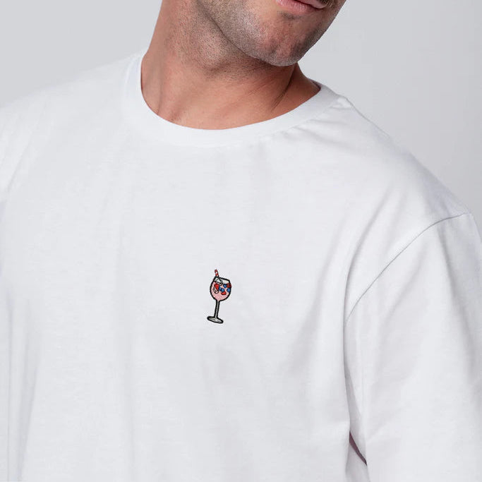 Ein Mann mit hellbraunem Haar und Schnurrbart trägt ein schlichtes weißes T-Shirt mit einem kleinen gestickten Cocktailglasmotiv auf der linken Brust. Er blickt leicht nach oben und nach rechts und hat einen neutralen Gesichtsausdruck.