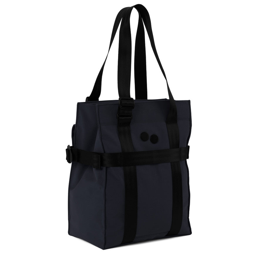 Eine dunkle, marineblaue Tragetasche mit schwarzen Trägern und einem schwarzen, horizontalen Band, das auf der Vorderseite zwei schwarze, runde Akzente aufweist. Die Tasche steht aufrecht, hat verstärkte Griffe und eine rechteckige Form.