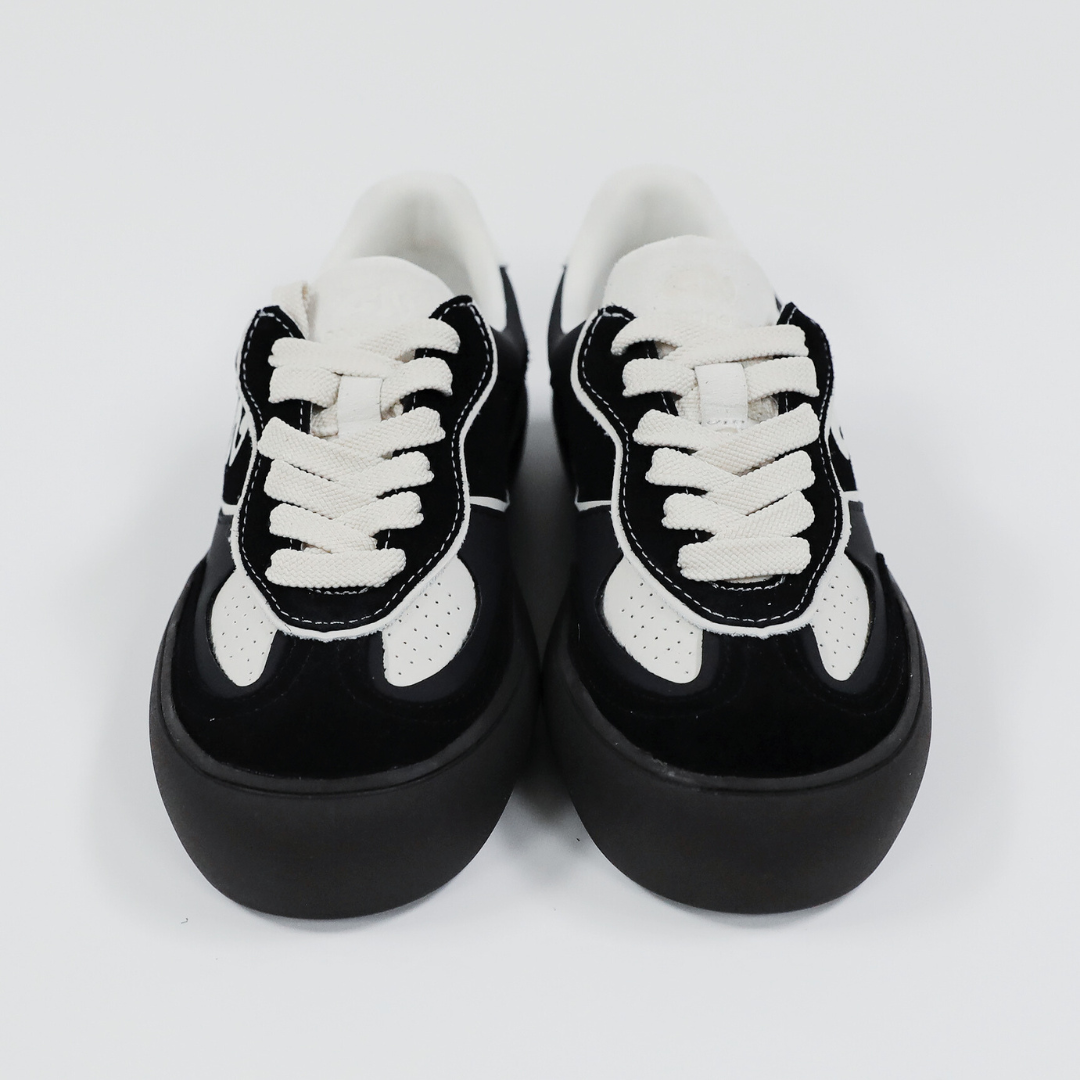 Schwarz-weiße Sneaker mit dicken Sohlen und weißen Schnürsenkeln auf weißem Hintergrund.