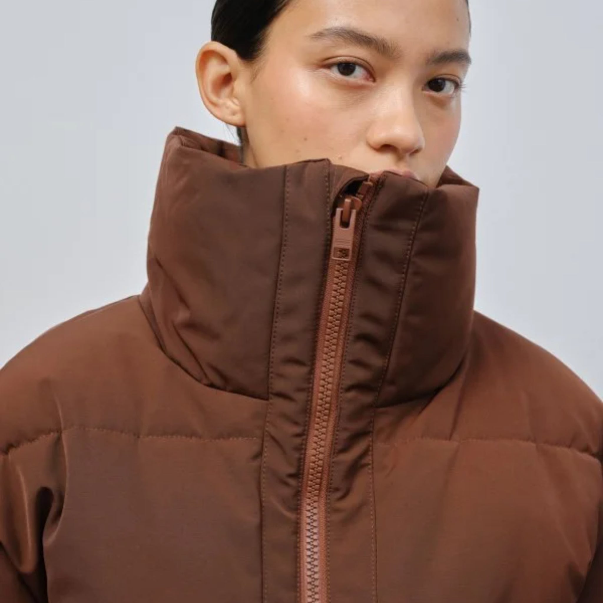 Eine Person trägt eine braune Jacke mit hohem Kragen und blickt in die Kamera.