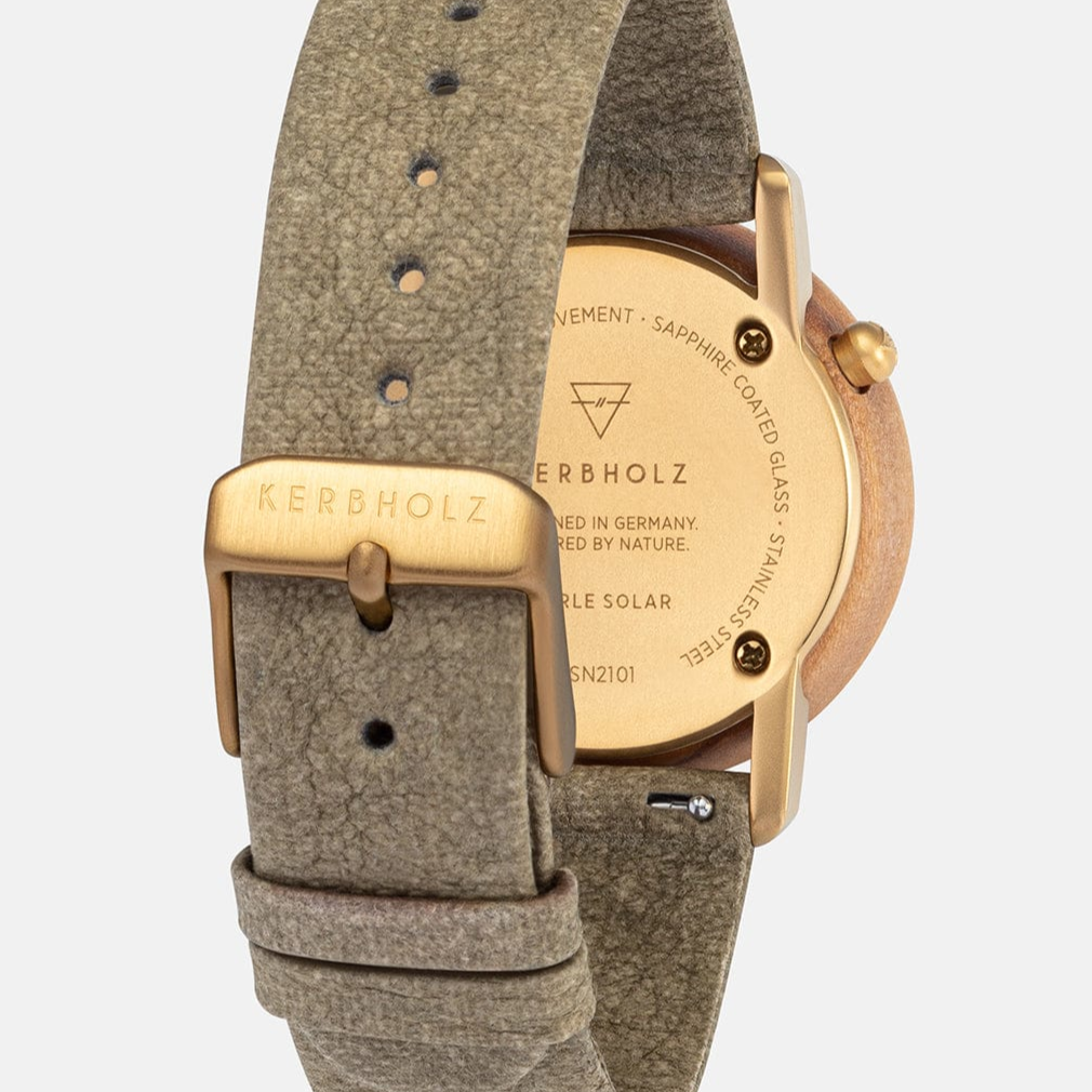 Rückseite einer Kerbholz-Uhr mit goldenem Gehäuse und grauem Lederarmband, Details auf dem Gehäuseboden sichtbar.
