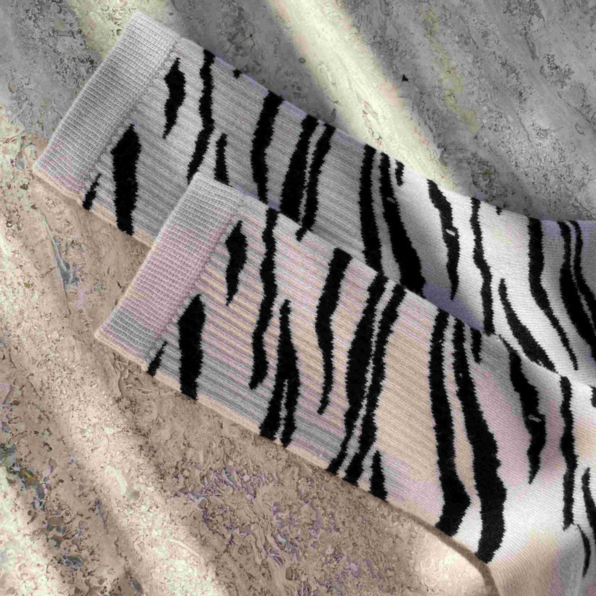 Ein Paar Socken mit schwarz-weißem Zebramuster liegt auf einer strukturierten, sonnenbeschienenen Oberfläche mit Licht- und Schattenstreifen.