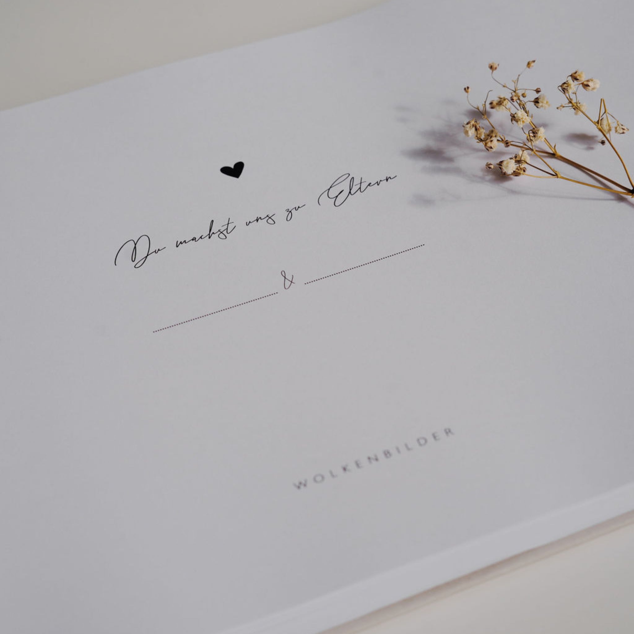 Das Bild zeigt ein Blatt Papier mit der Aufschrift "Du machst uns zu Eltern" und einem kleinen gepressten Blumensträußchen.