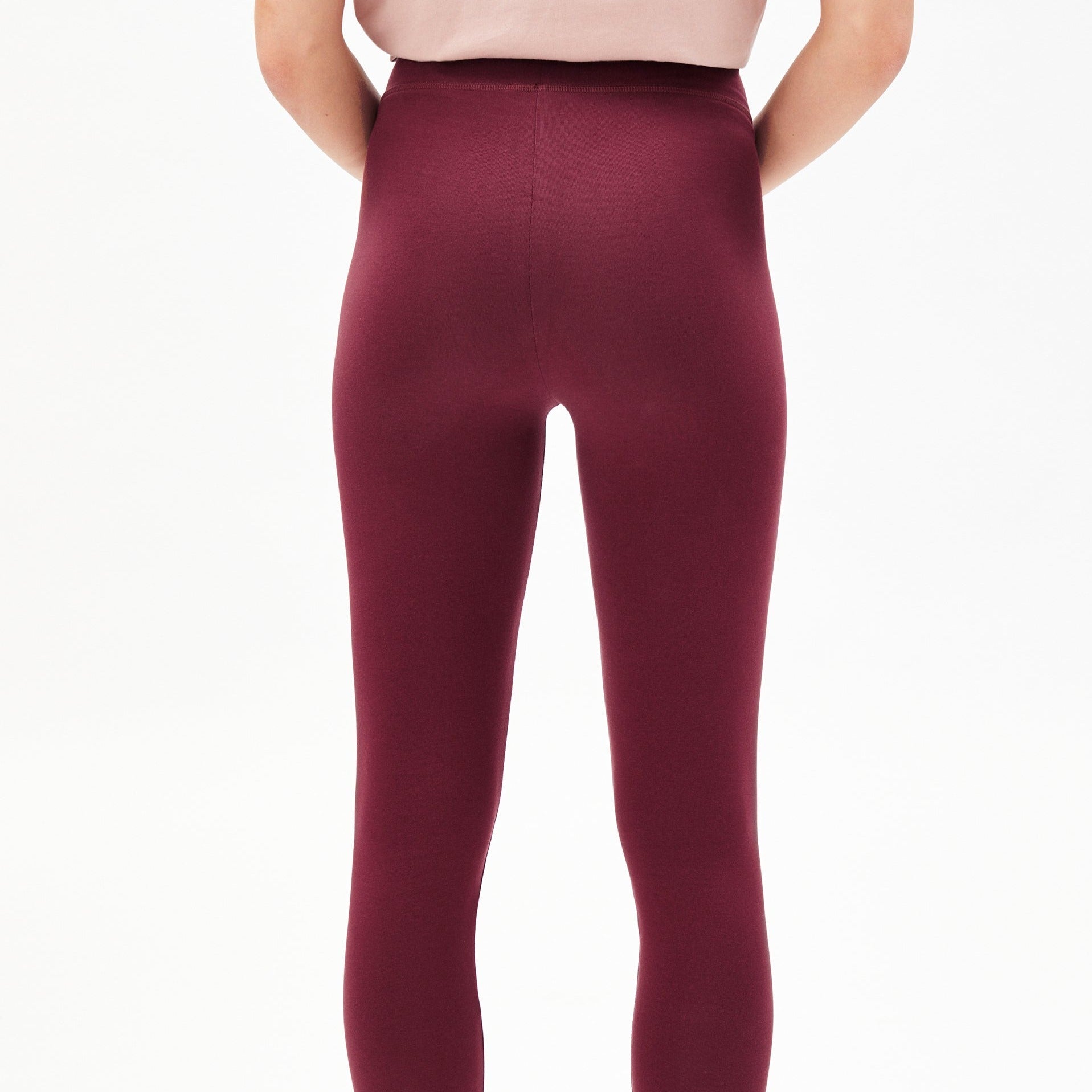 Eine Person trägt eine weinrote Leggings und ein rosa Oberteil, nur von hinten zu sehen.