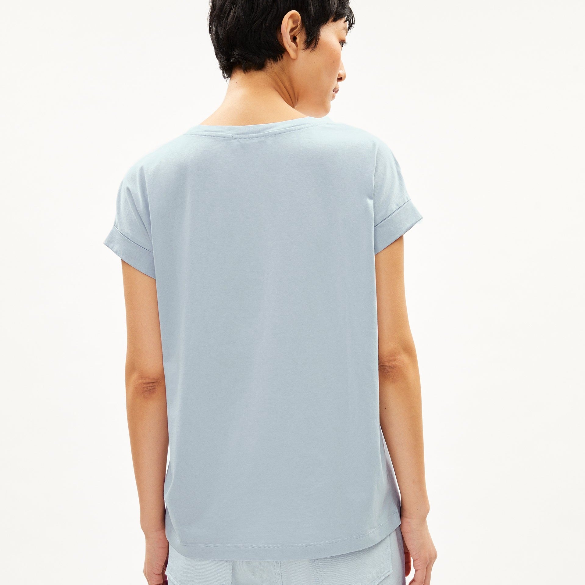 Eine Person mit kurzem Haar trägt ein hellblaues T-Shirt und steht mit dem Rücken zur Kamera.