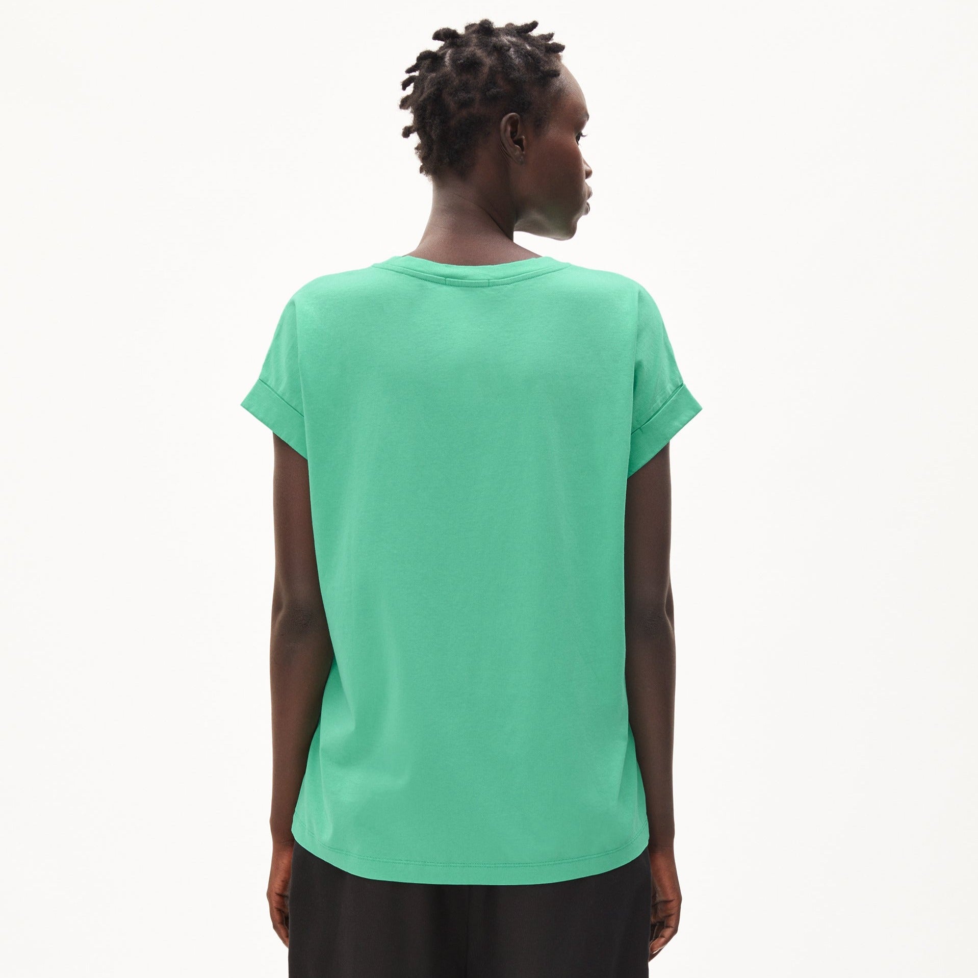 Person in grünen T-Shirt von hinten, mit kurzen Ärmeln, schaut zur Seite vor neutralem Hintergrund.