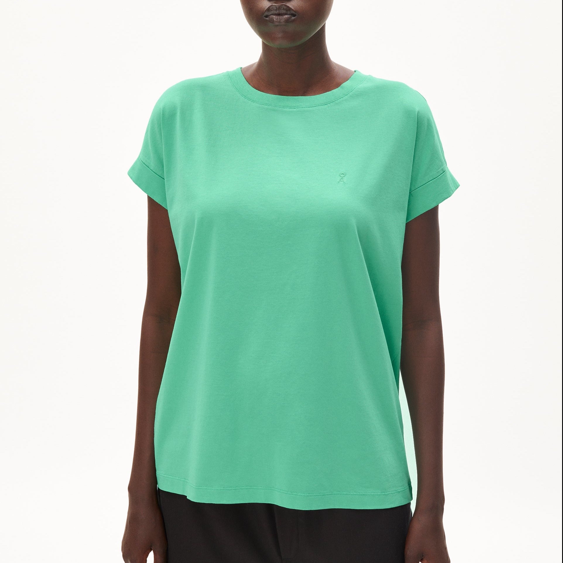 Person trägt ein lockeres, grünes T-Shirt mit hochgekrempelten Ärmeln vor weißem Hintergrund.