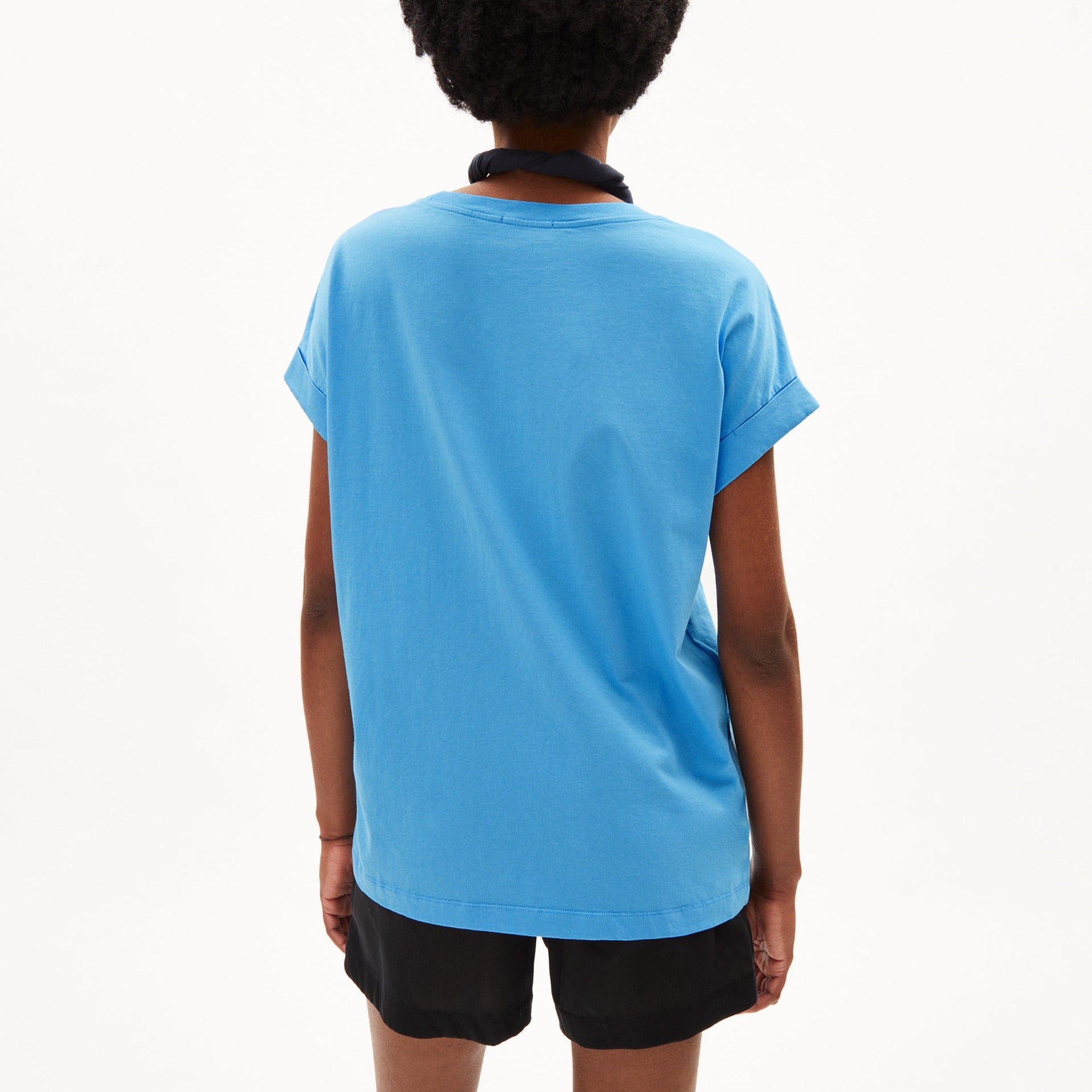 Person von hinten in einem blauen T-Shirt und schwarzen Shorts, steht vor einem weißen Hintergrund.