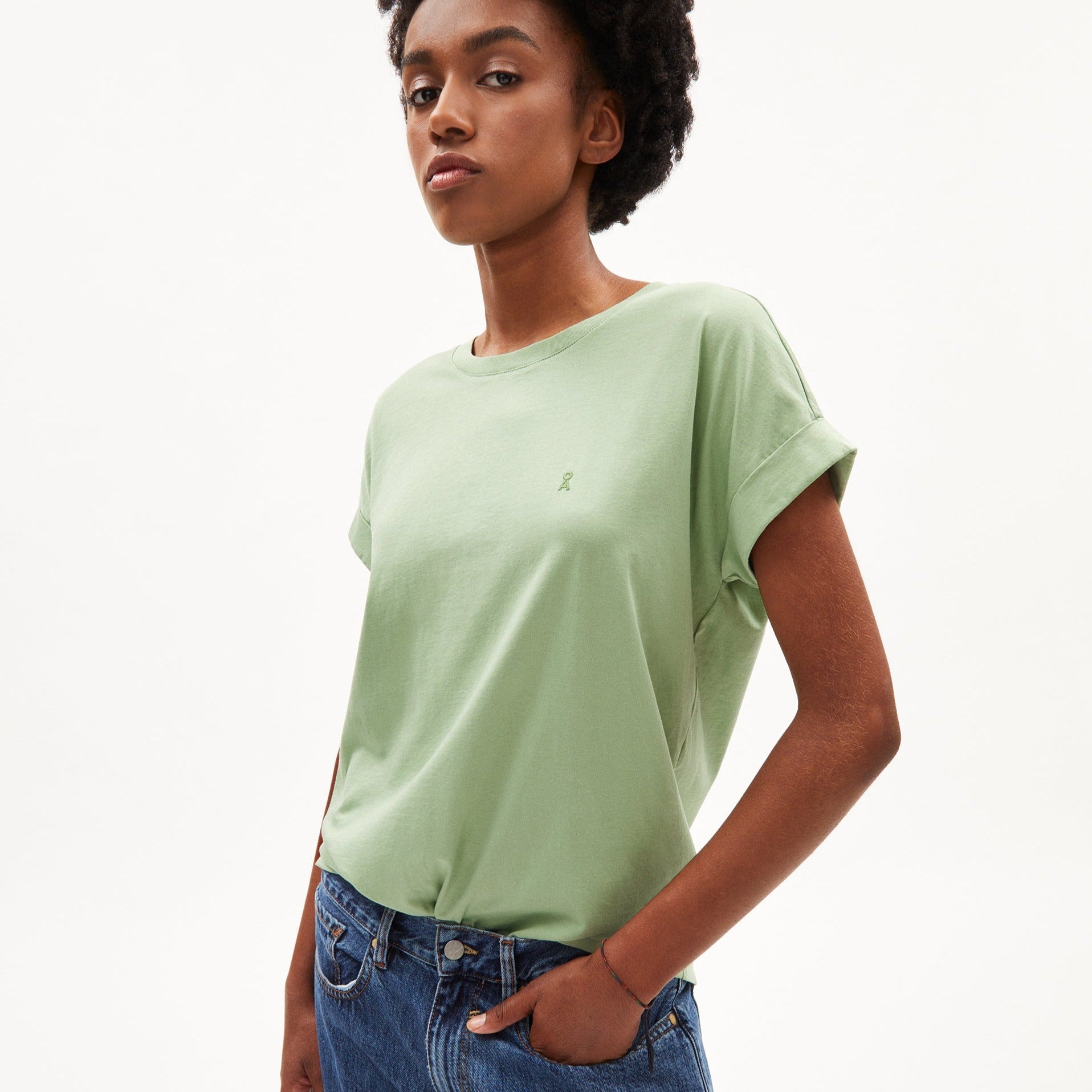 Person in grünem T-Shirt und blauer Jeans vor weißem Hintergrund.