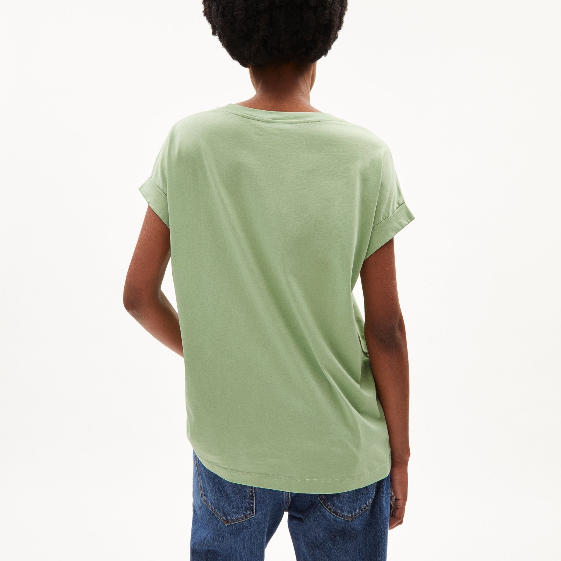 Person von hinten in einem hellgrünen T-Shirt und blauer Jeans vor einem weißen Hintergrund.