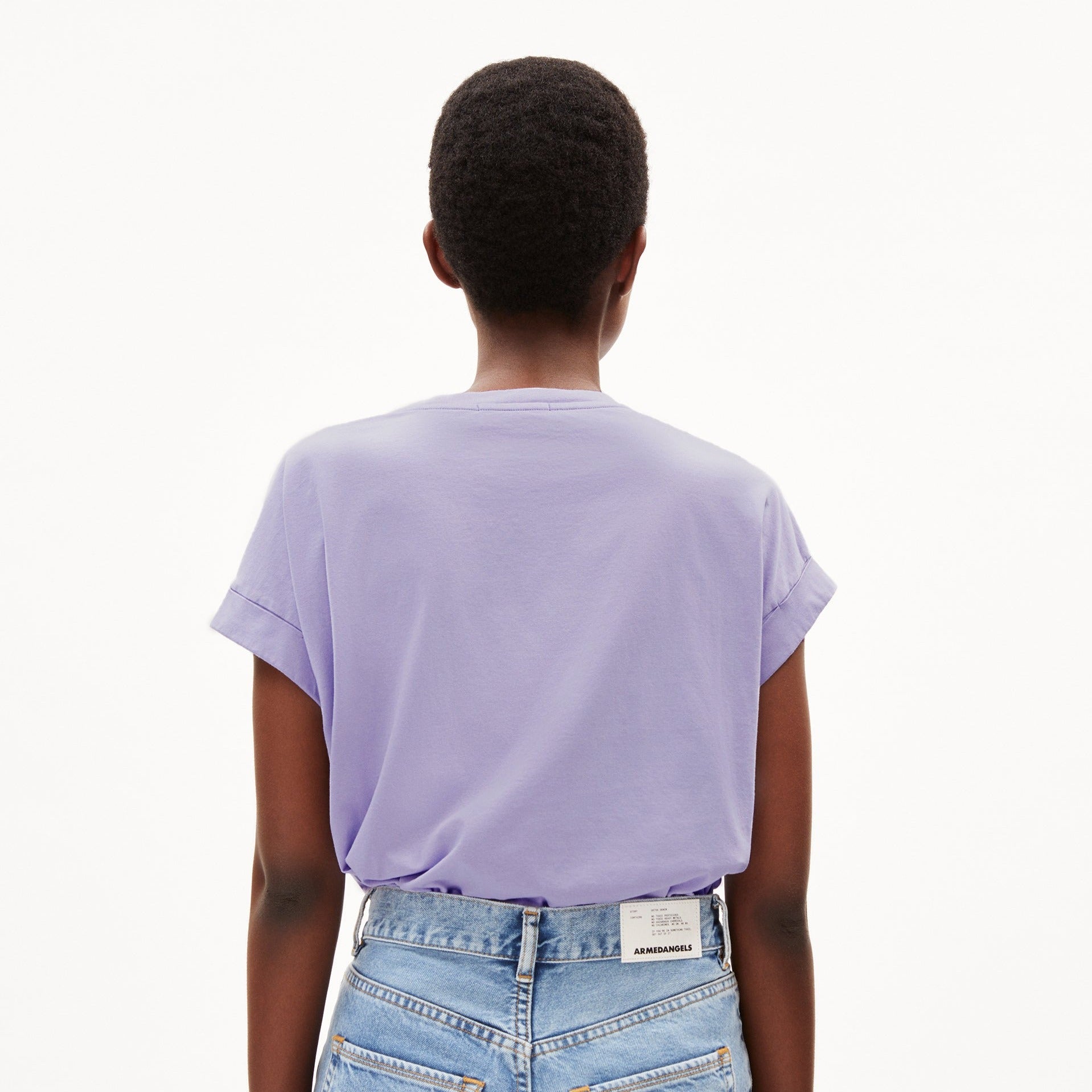 Person von hinten in lila T-Shirt und blauer Jeans, vor weißem Hintergrund.