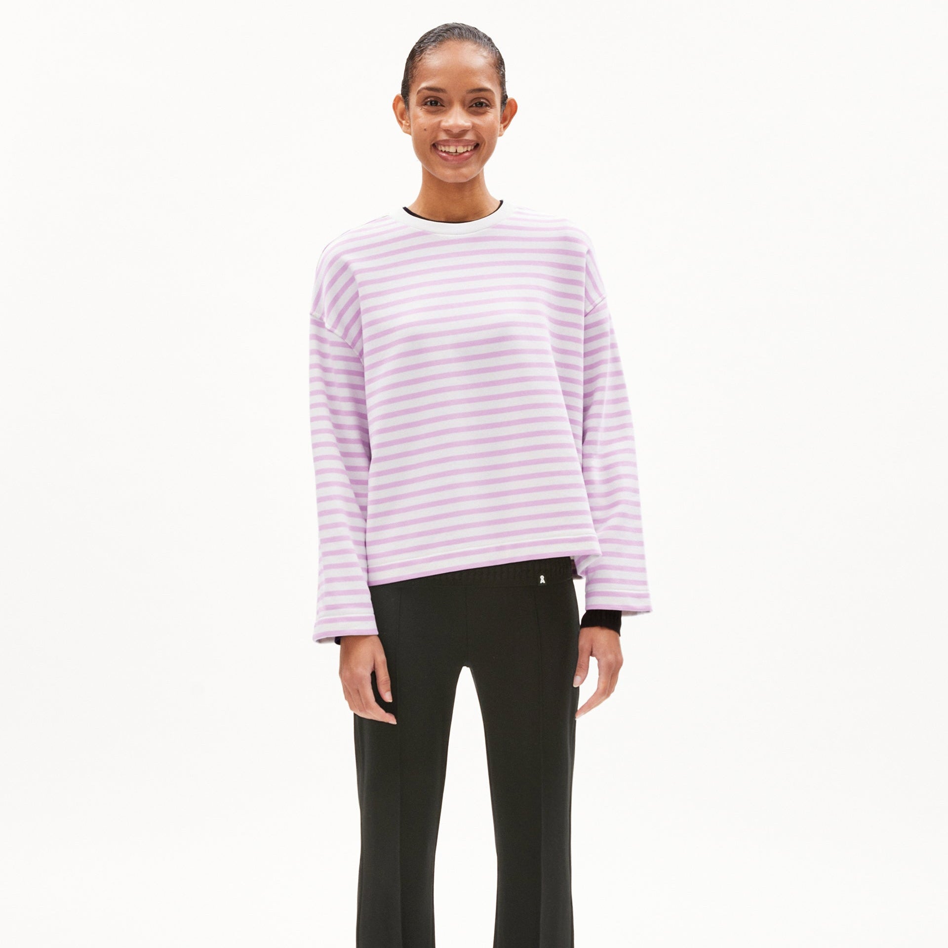 Person in a purple and white striped sweater and black pants smiles against a plain white background.