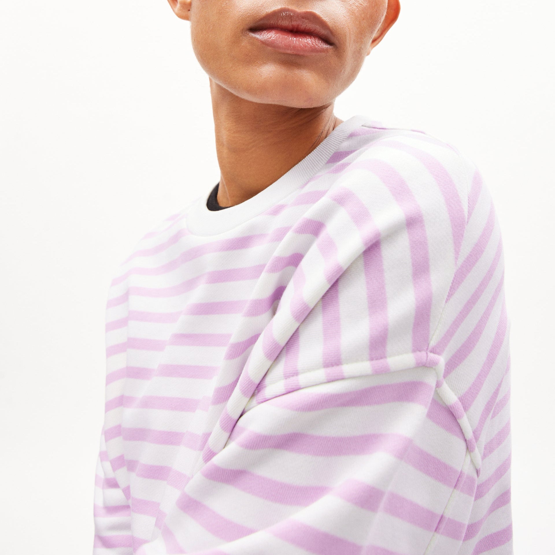 Person in lila-weiß gestreiftem Langarm-Shirt, Nahaufnahme des Oberkörpers und Gesichts, vor hellem Hintergrund.