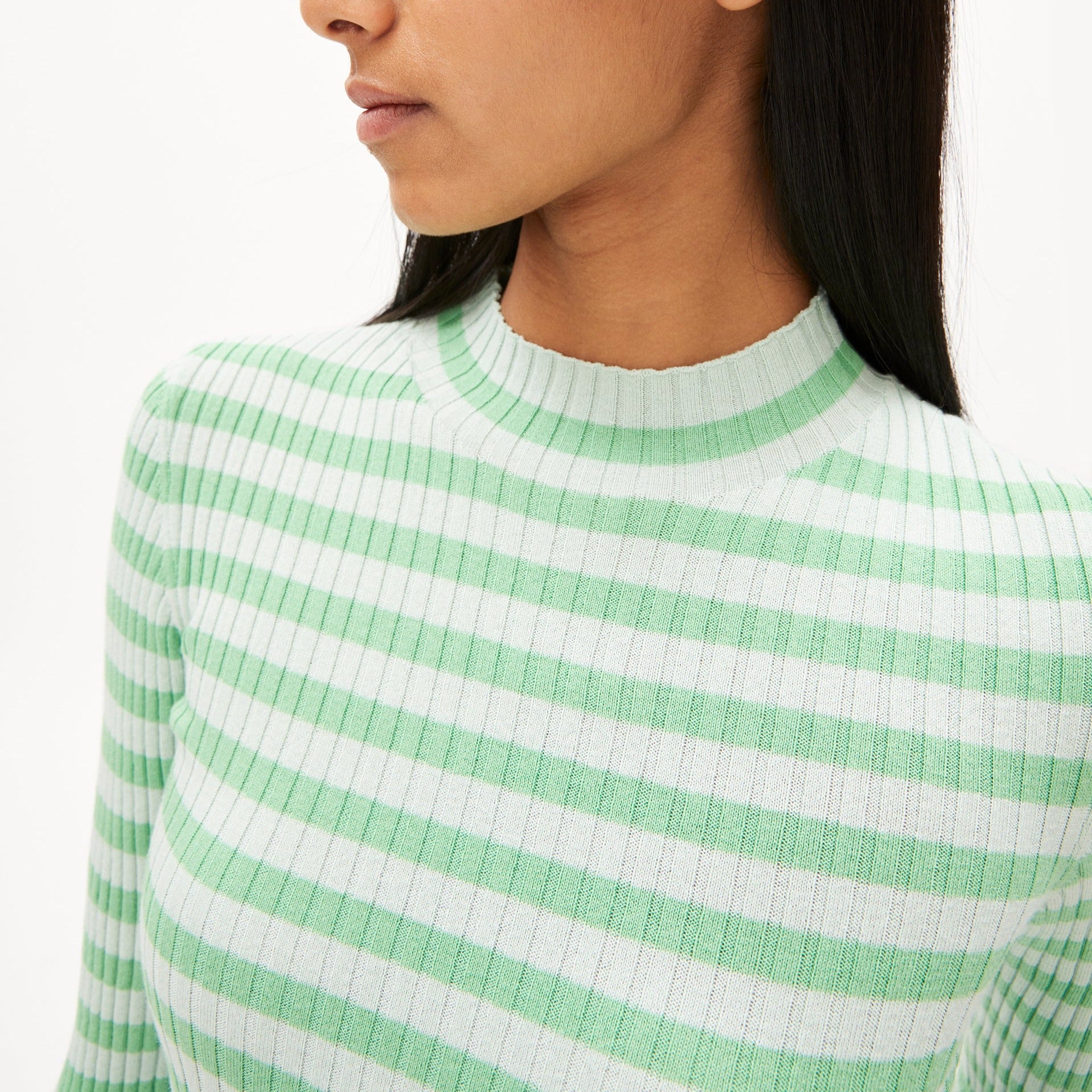 Person in gestreiftem Pullover mit grünen und weißen Streifen, Kopf leicht zur Seite gedreht.