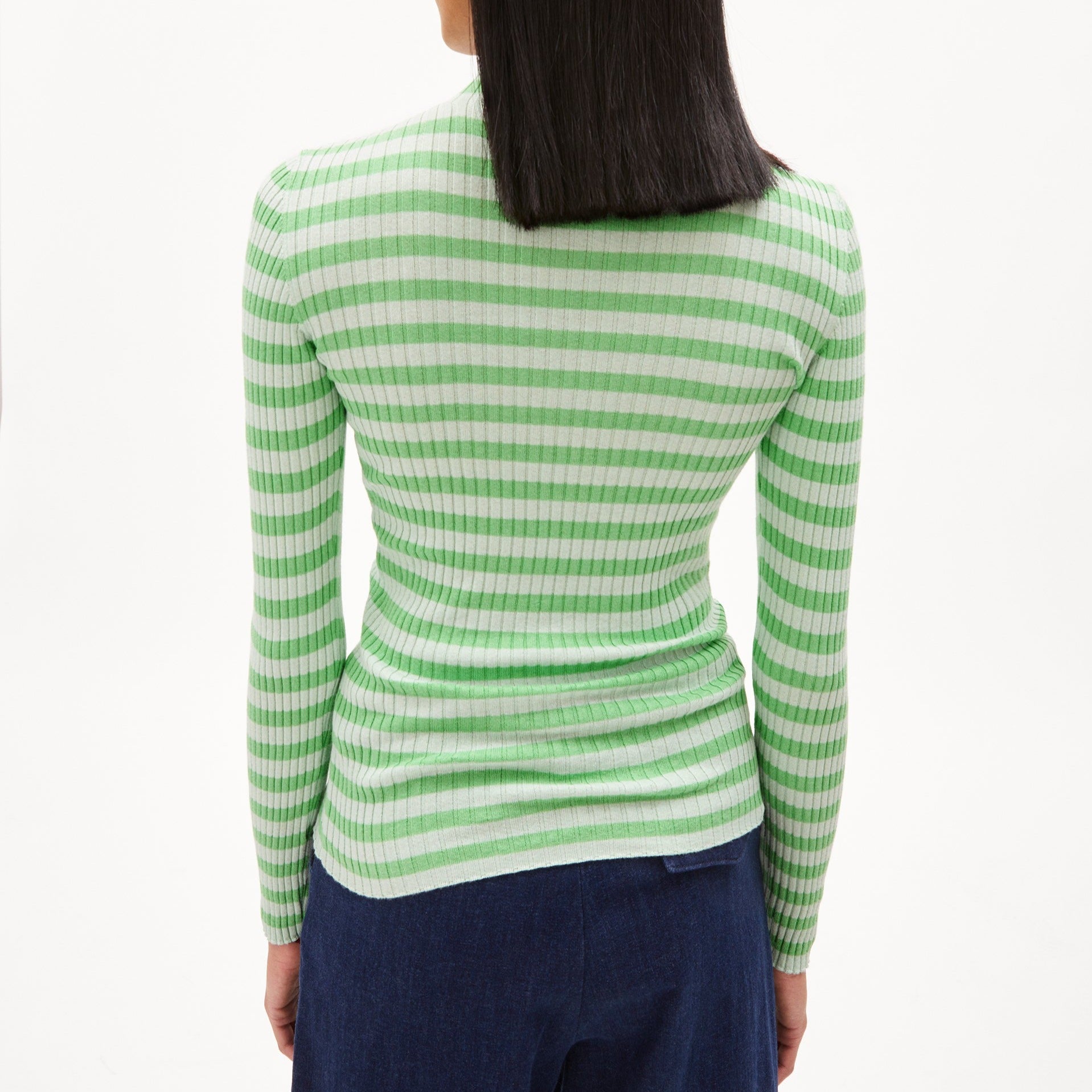 Eine Person mit schulterlangem Haar trägt ein gestreiftes grünes Oberteil und dunkelblaue Hose, von hinten gesehen.