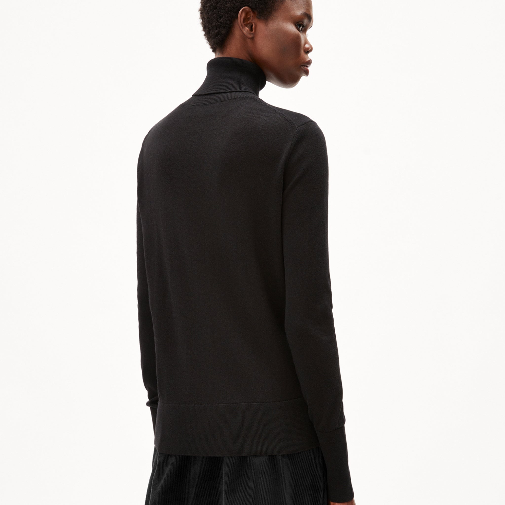 Person in schwarzem Rollkragenpullover schaut von der Seite weg, vor weißem Hintergrund.