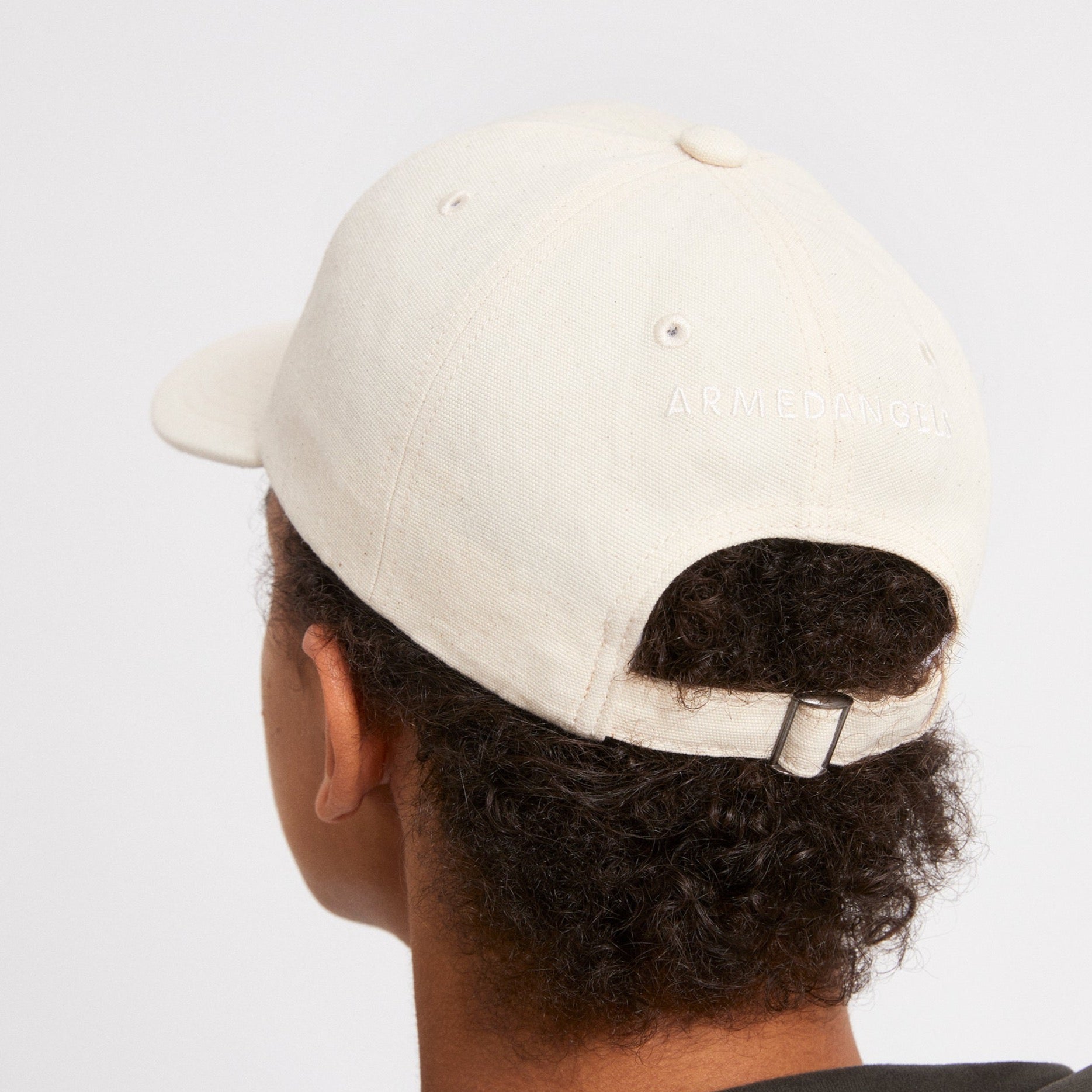 Person mit einer hellen Baseballkappe von hinten, mit der Aufschrift "Armedangels" auf der Kappe.