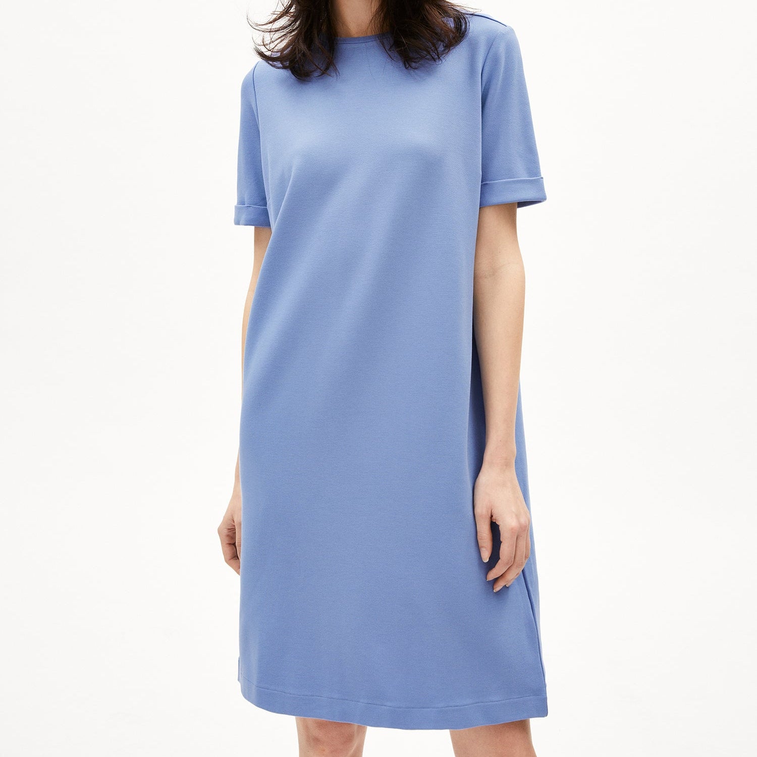 Eine Frau trägt ein schlichtes, blaues T-Shirt-Kleid und steht vor einem weißen Hintergrund.