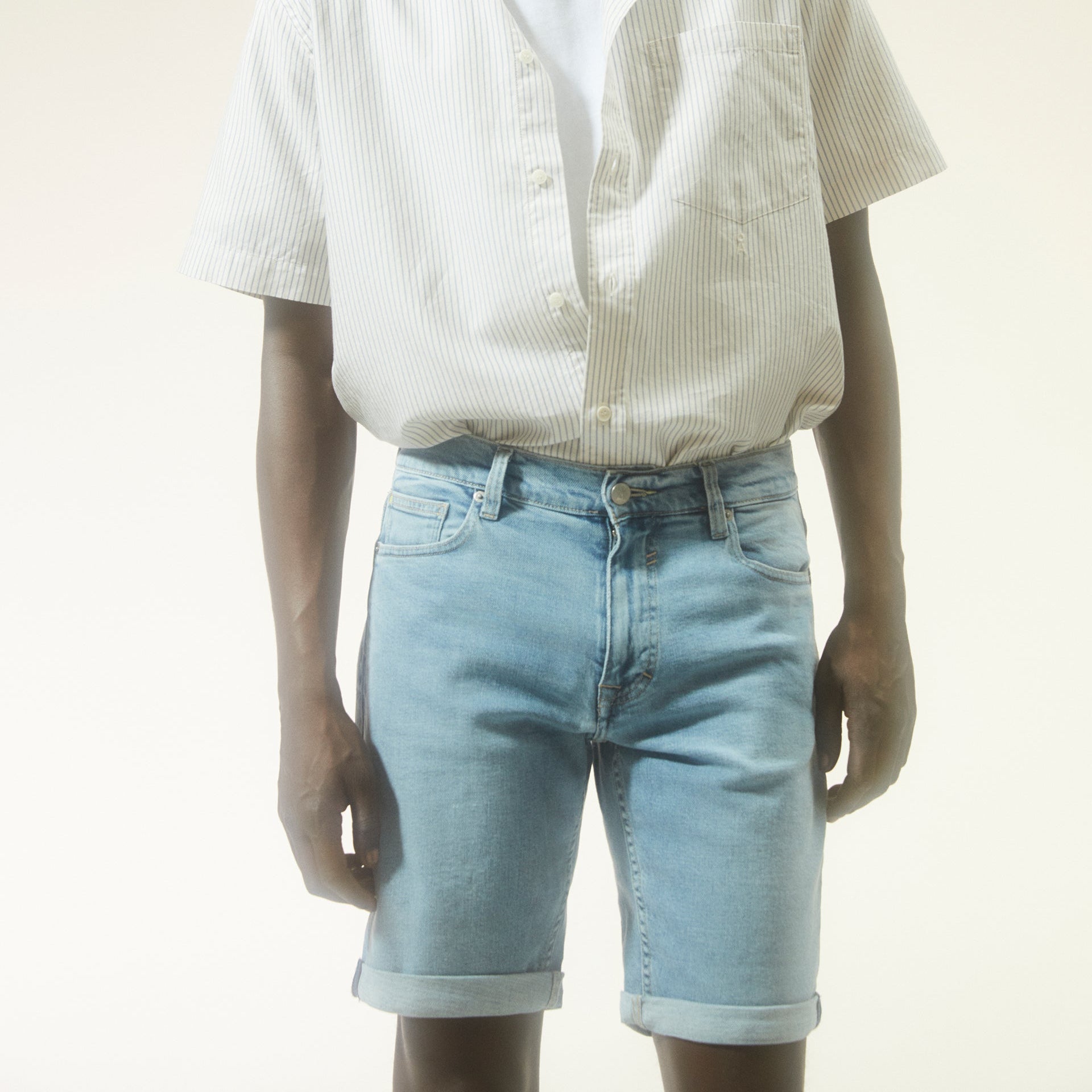 Person in a short-sleeved, striped shirt and light blue denim shorts against a neutral background.