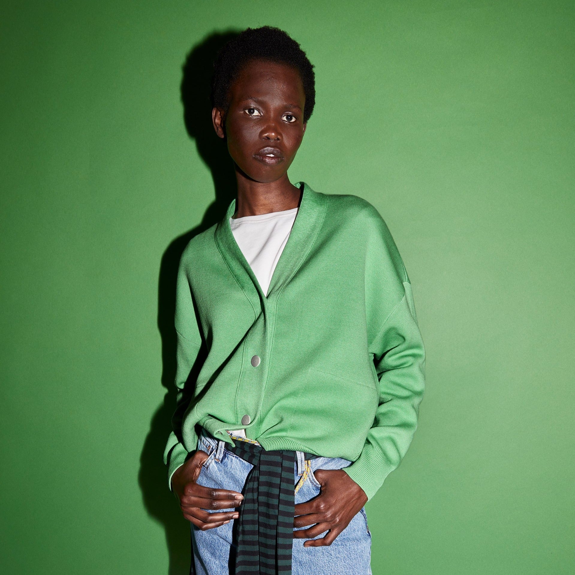 Person in grüner Strickjacke und Jeans vor einem grünen Hintergrund.