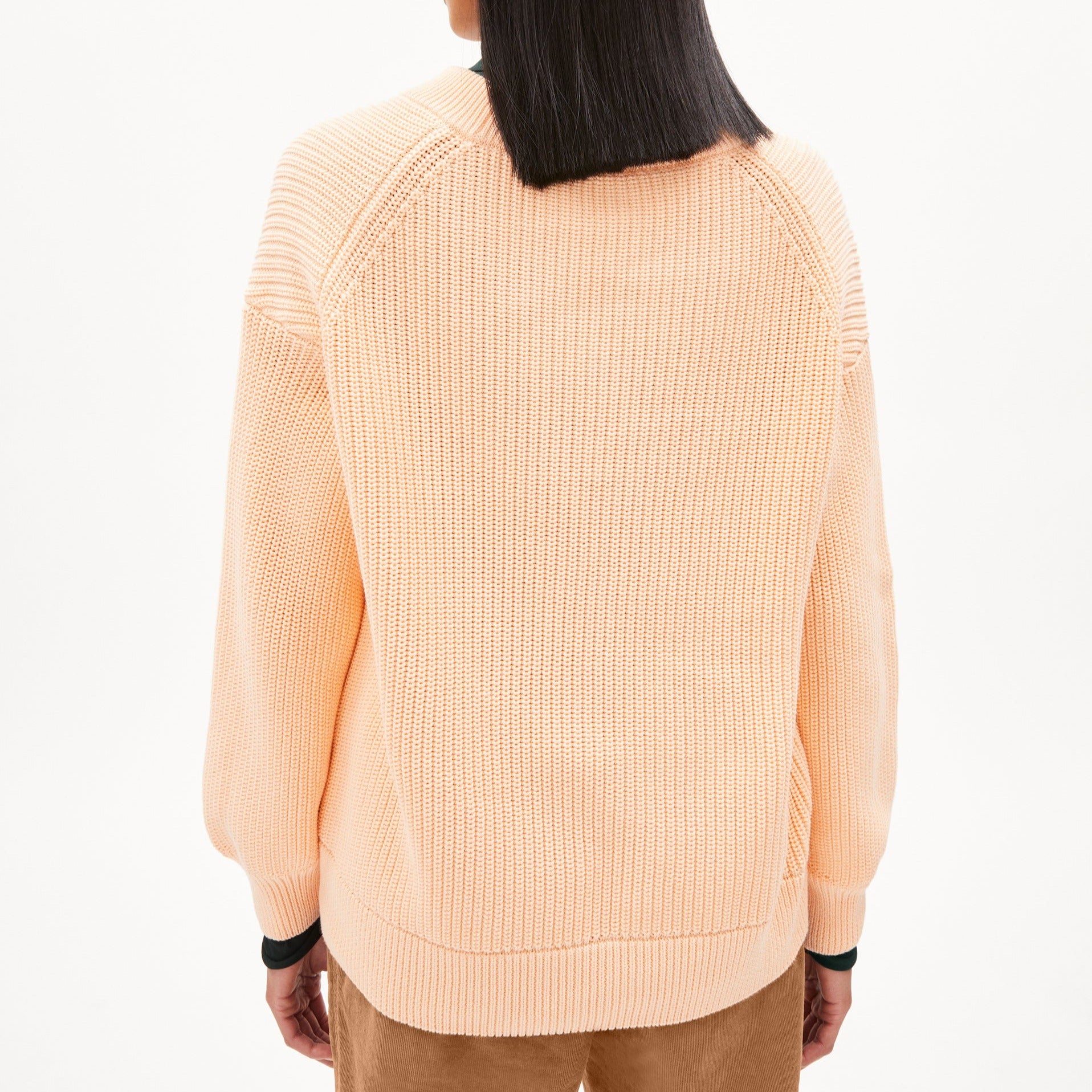 Person von hinten in einem pfirsichfarbenen Strickpullover und beigefarbenen Hose.
