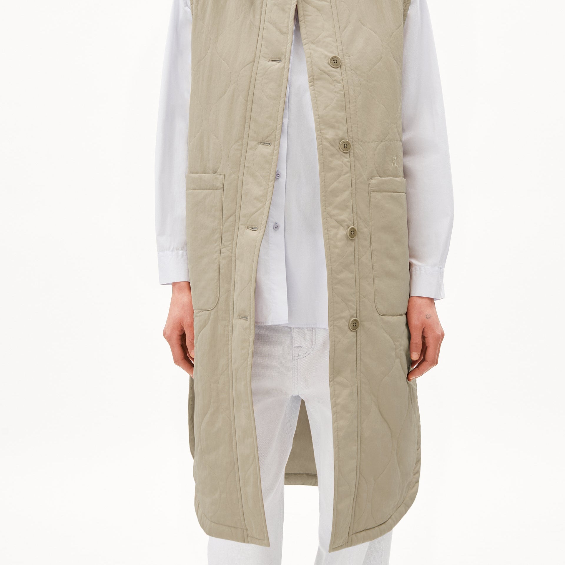 Person in weißem Hemd und hellgrauer, gesteppter, ärmelloser Weste, die bis zu den Knien reicht.